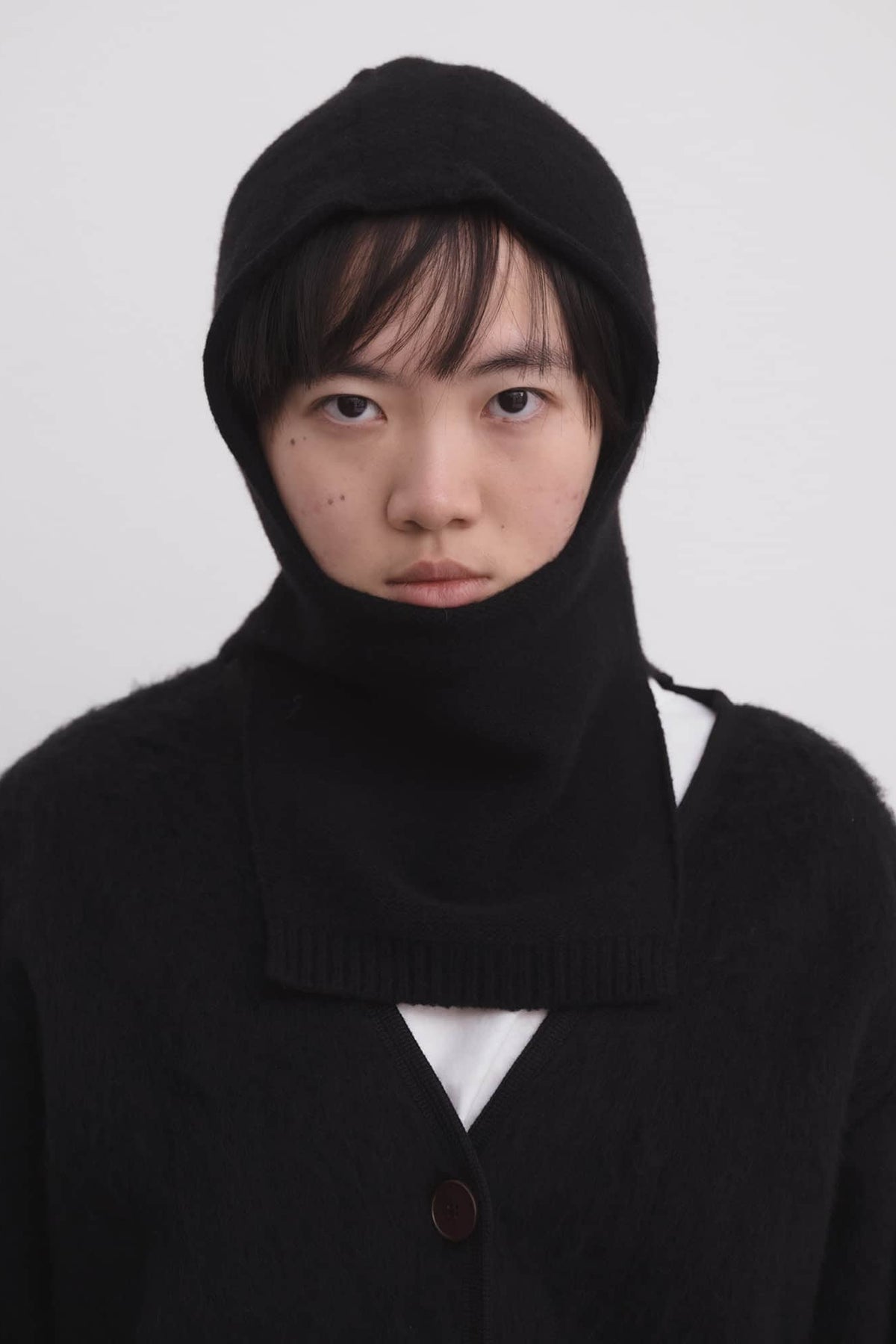 Person wearing a black knit outfit with a hood against a white background