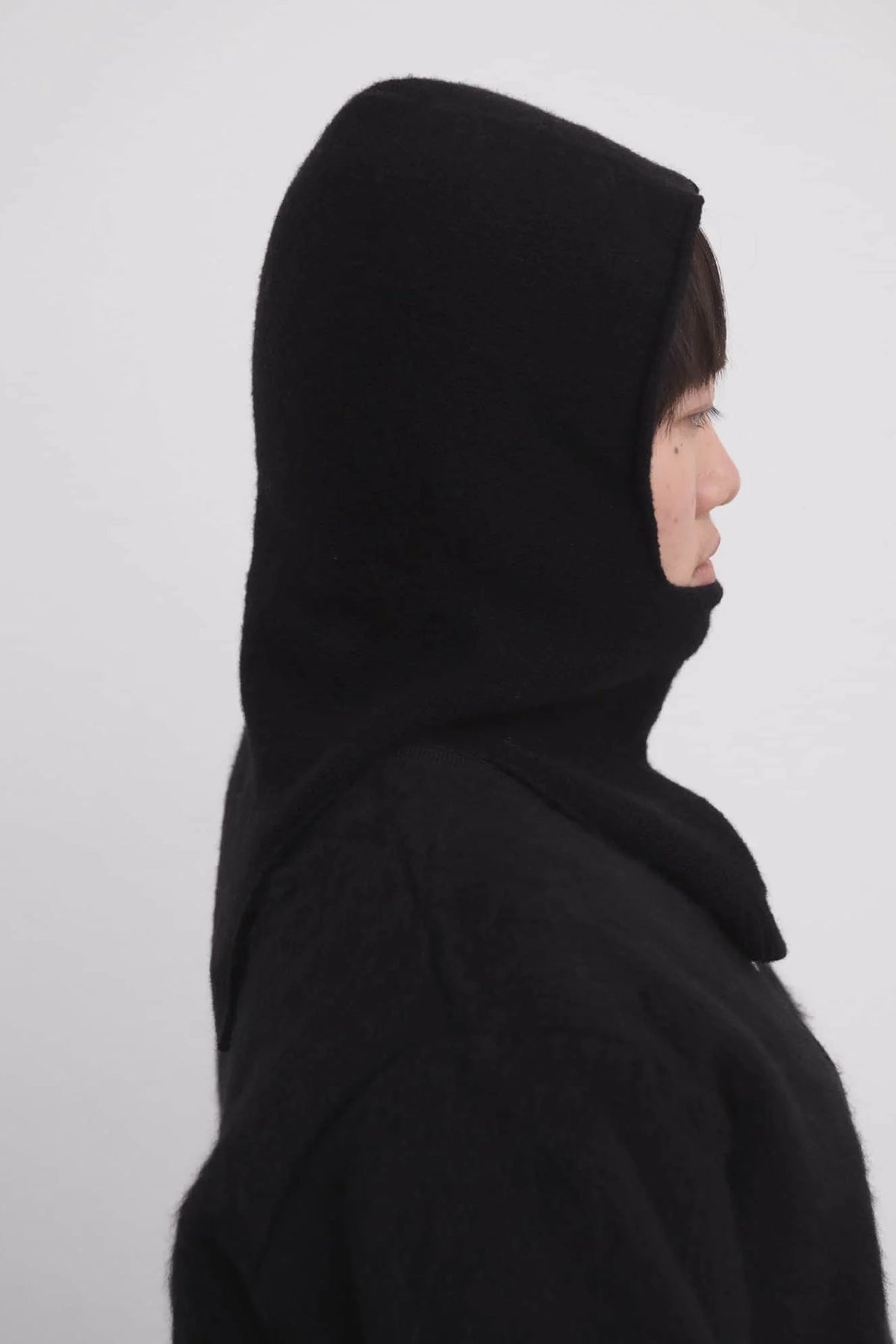 Person wearing a black hooded garment against a white background