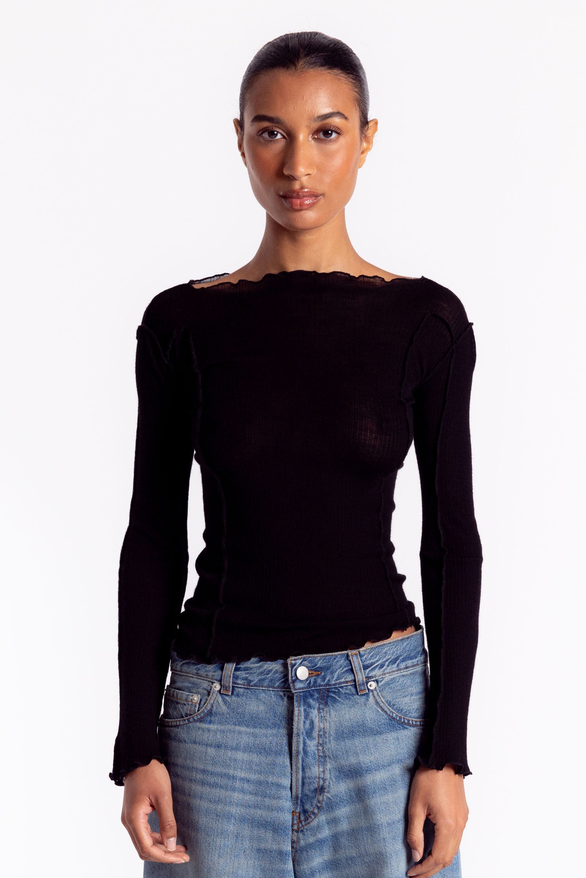 Woman wearing a black long-sleeve top and blue jeans on a white background