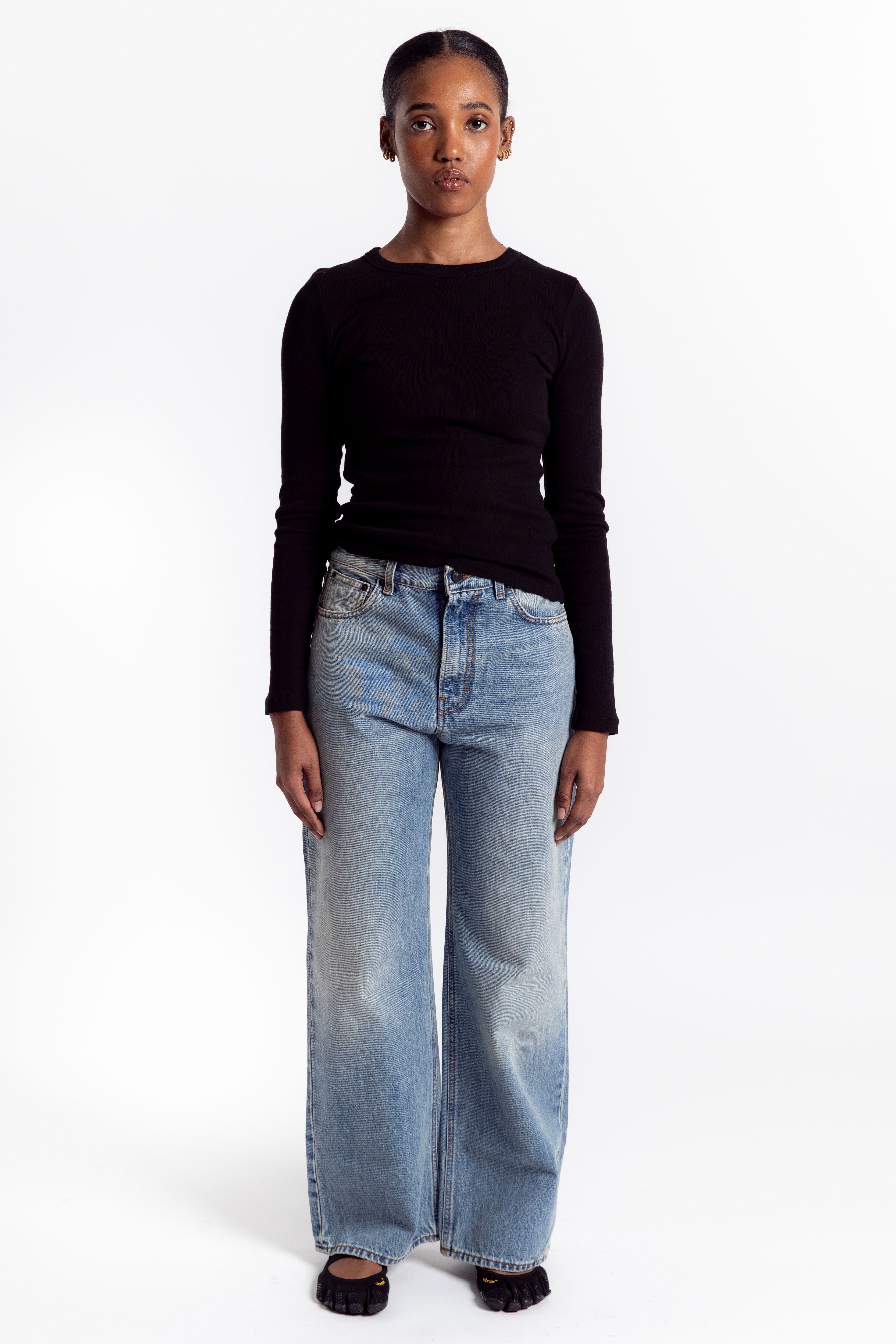Person wearing a black long-sleeve top and light blue jeans on a white background