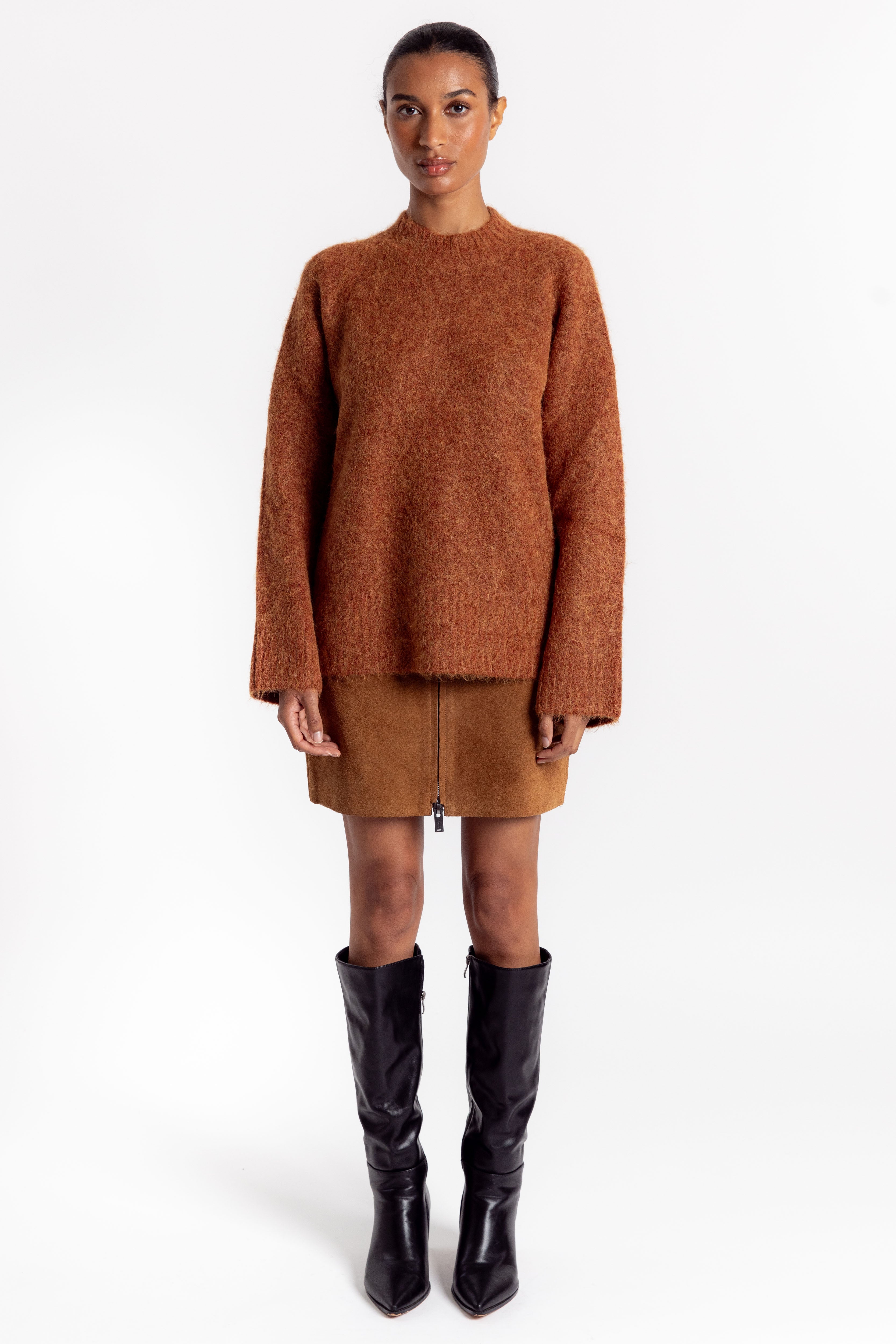 Woman wearing a brown sweater and skirt with black knee-high boots on a white background