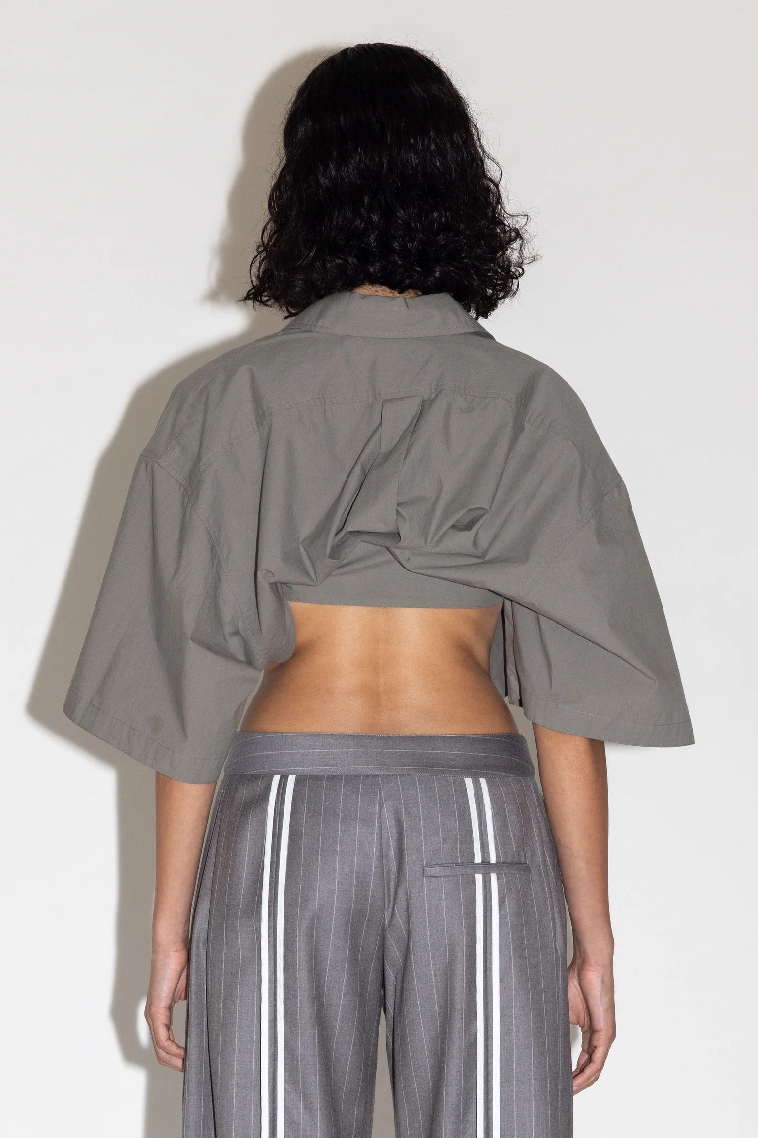 Person wearing a gray cropped jacket and gray pants with white stripes on a plain background