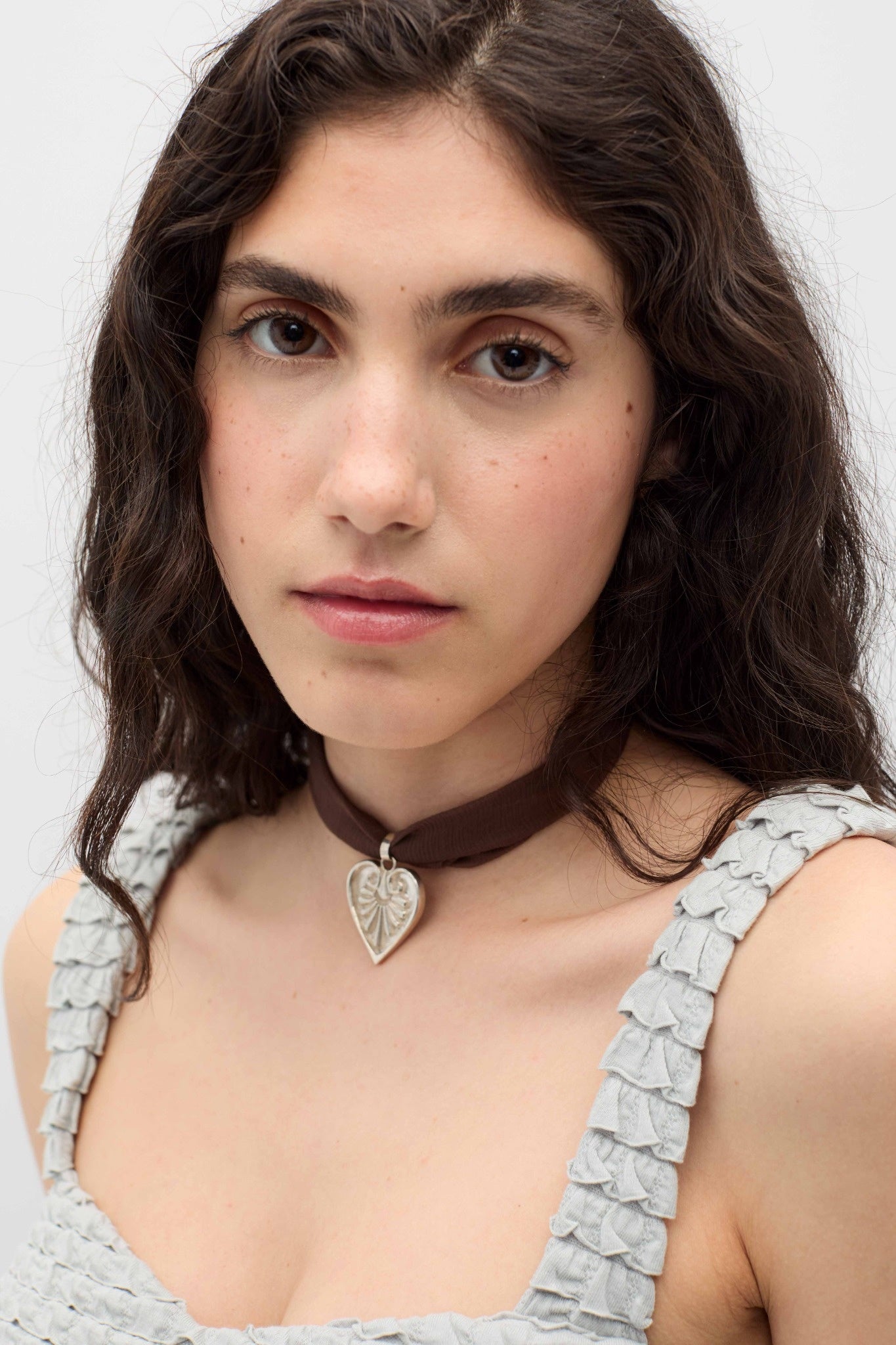 Woman wearing a silver necklace with a heart pendant against a plain background