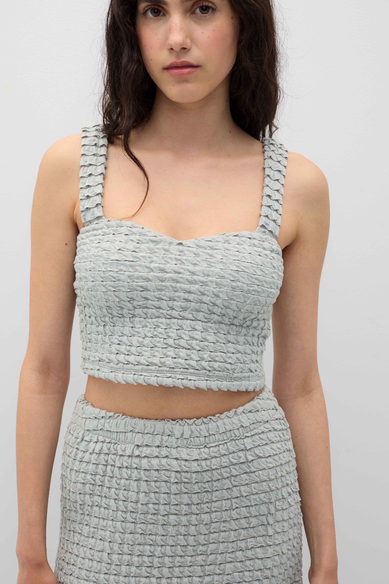 Woman wearing a textured gray top and skirt set against a plain background