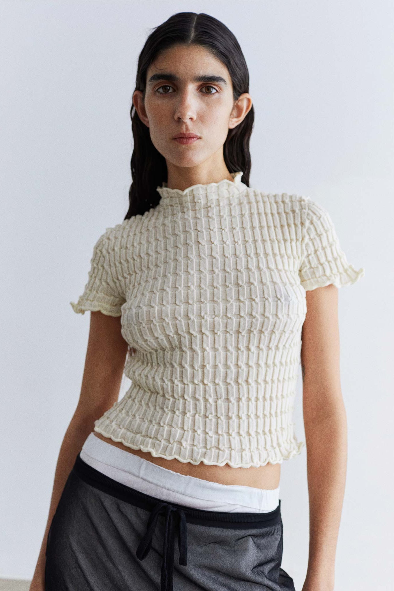 Woman wearing a textured white top against a plain background