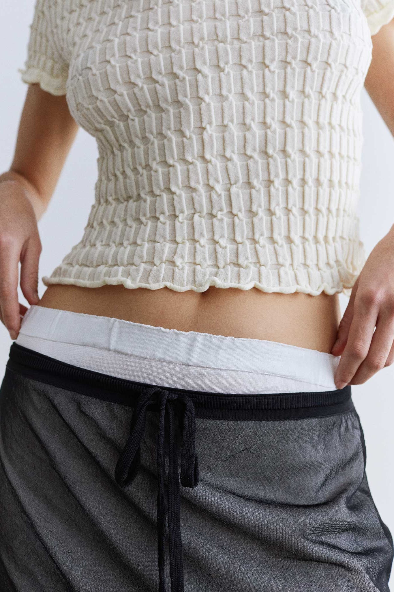 Person wearing a textured white top and gray pants on a plain background