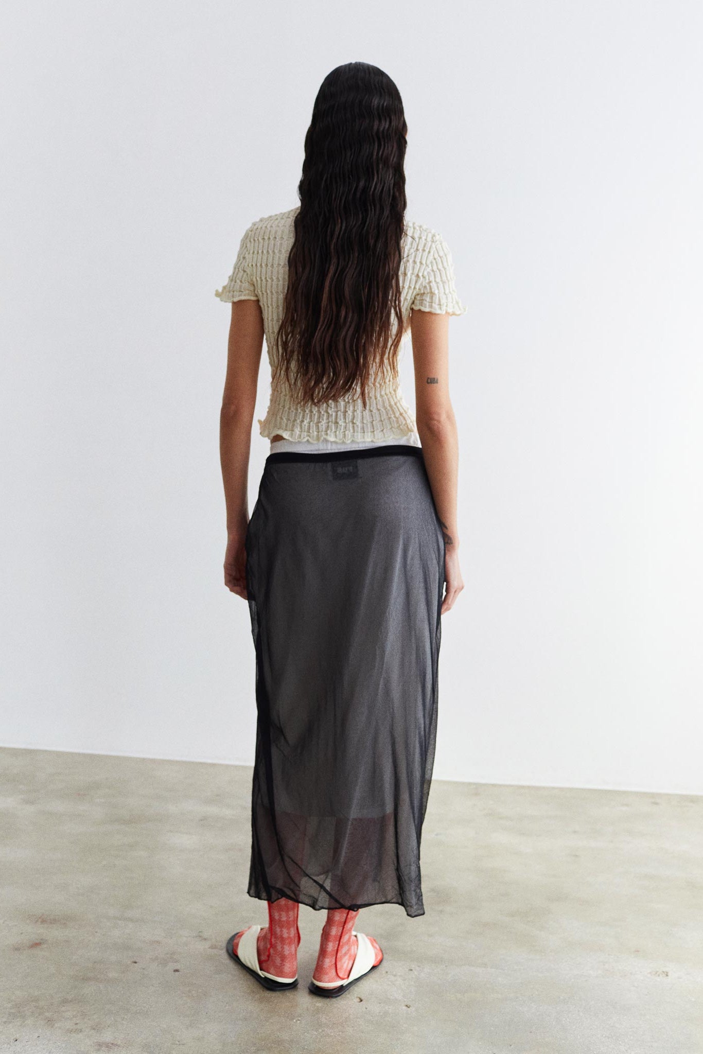 Person wearing a long dark skirt and white top against a plain background