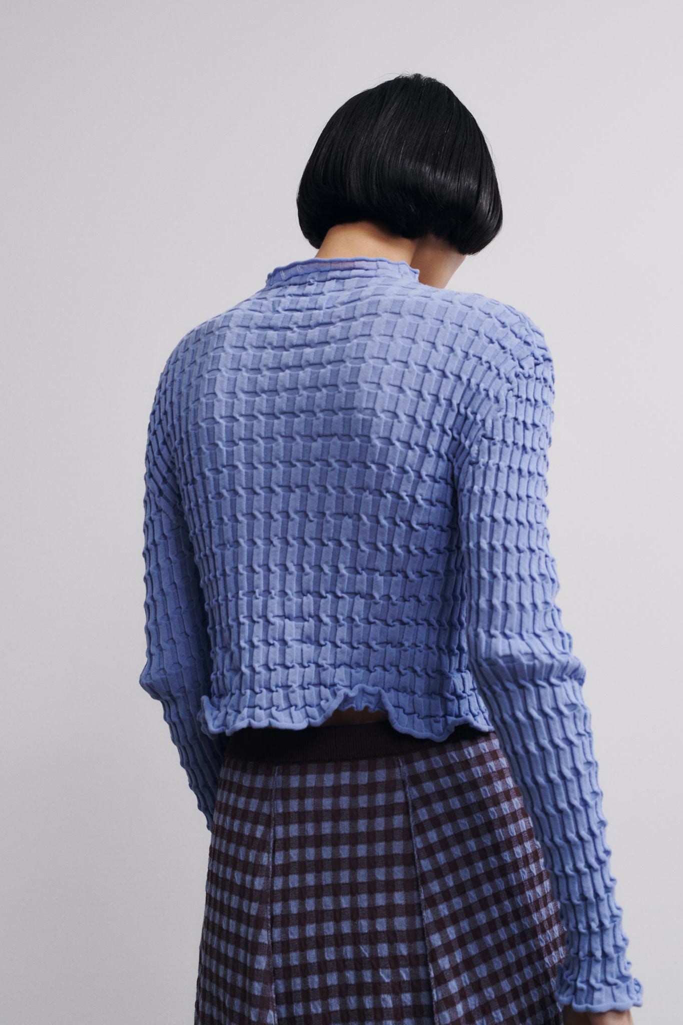 Person wearing a textured blue sweater and plaid skirt on a plain background