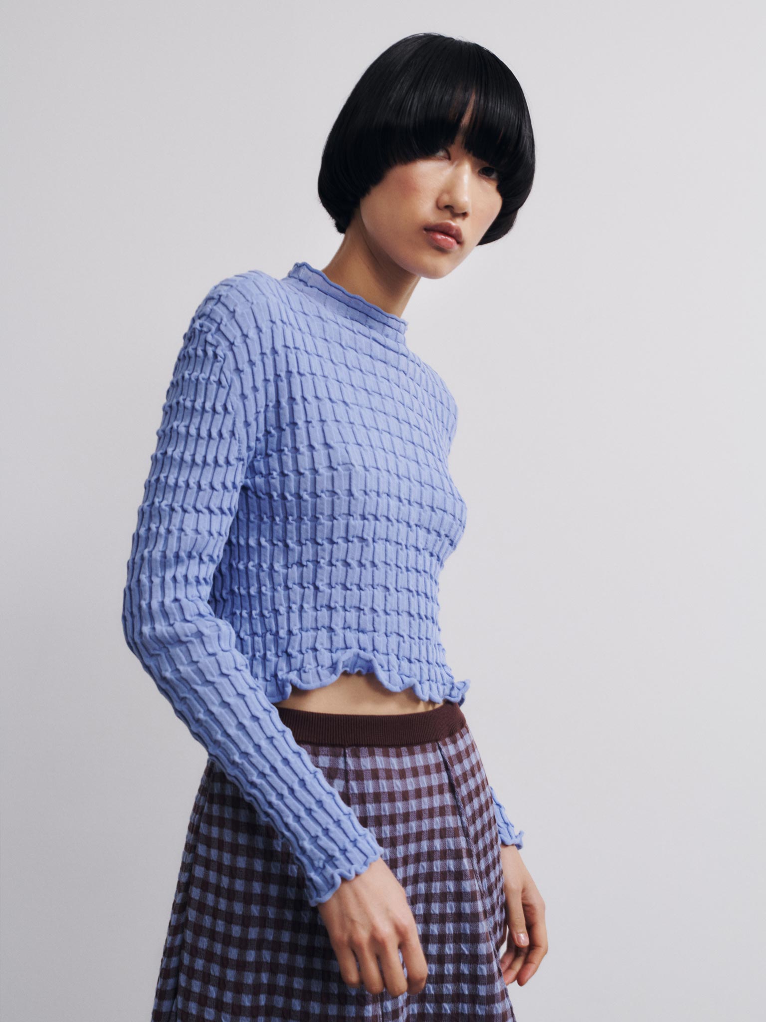 Person wearing a textured blue sweater and plaid skirt on a plain background