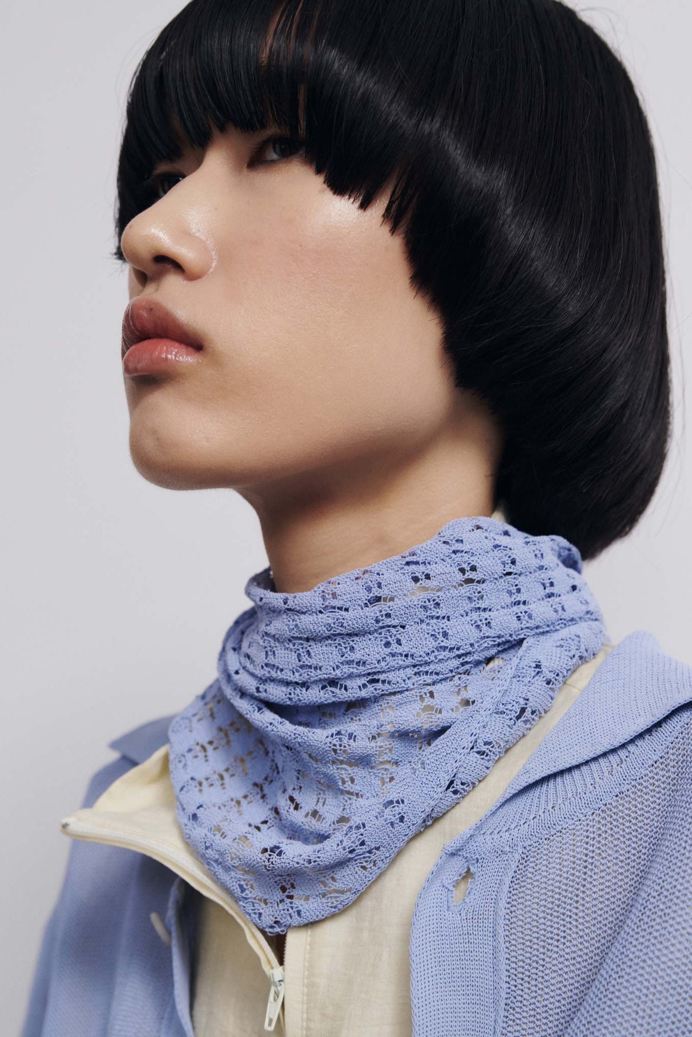 Person wearing a light blue scarf with a subtle pattern on a plain background