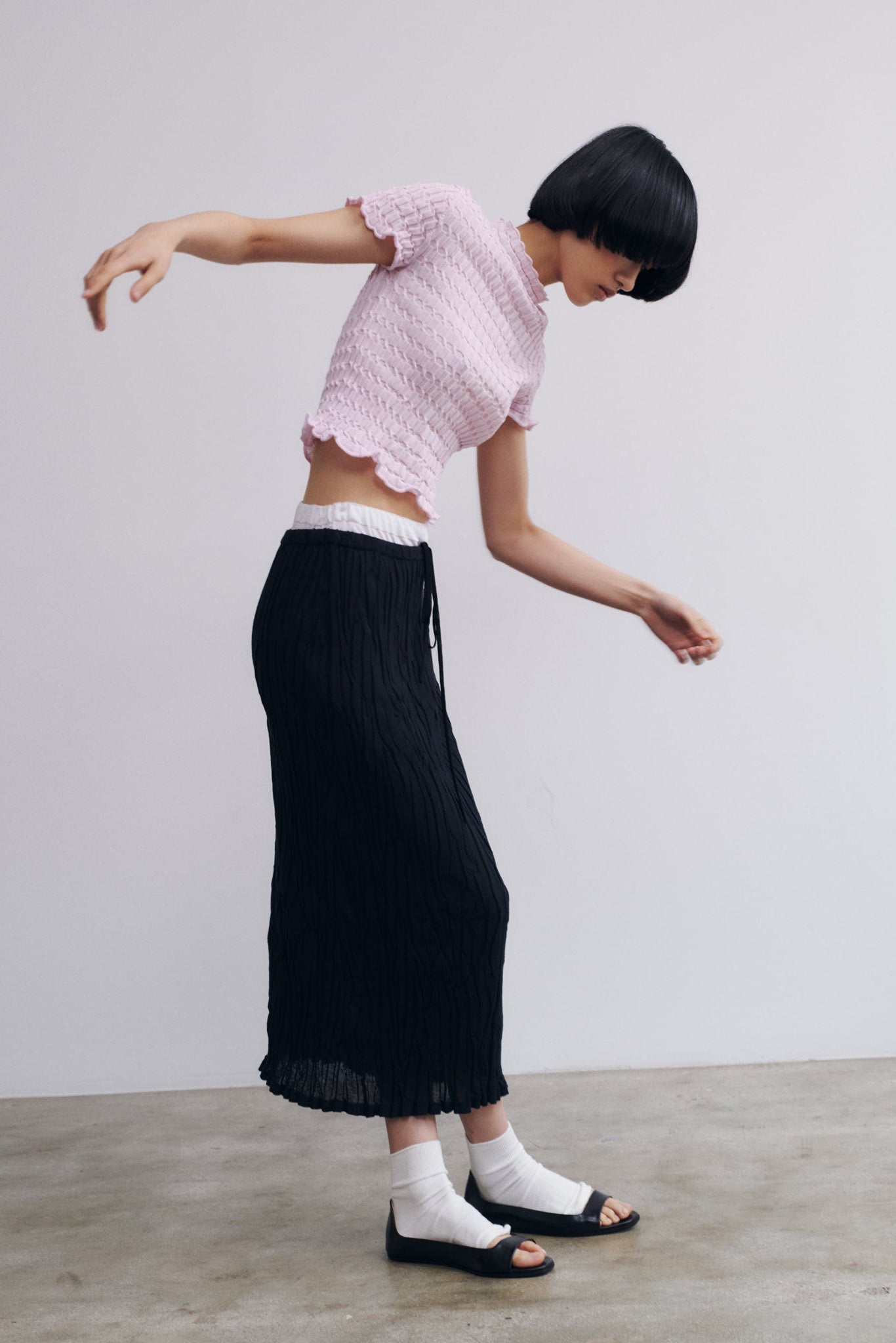 Person wearing a pink top and black pants on a plain background