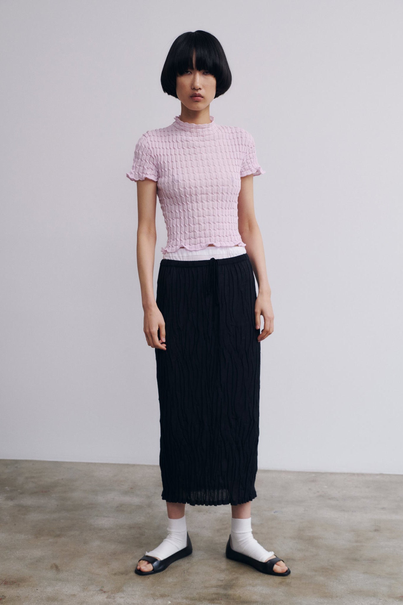 Person wearing a pink textured top and black skirt against a plain background