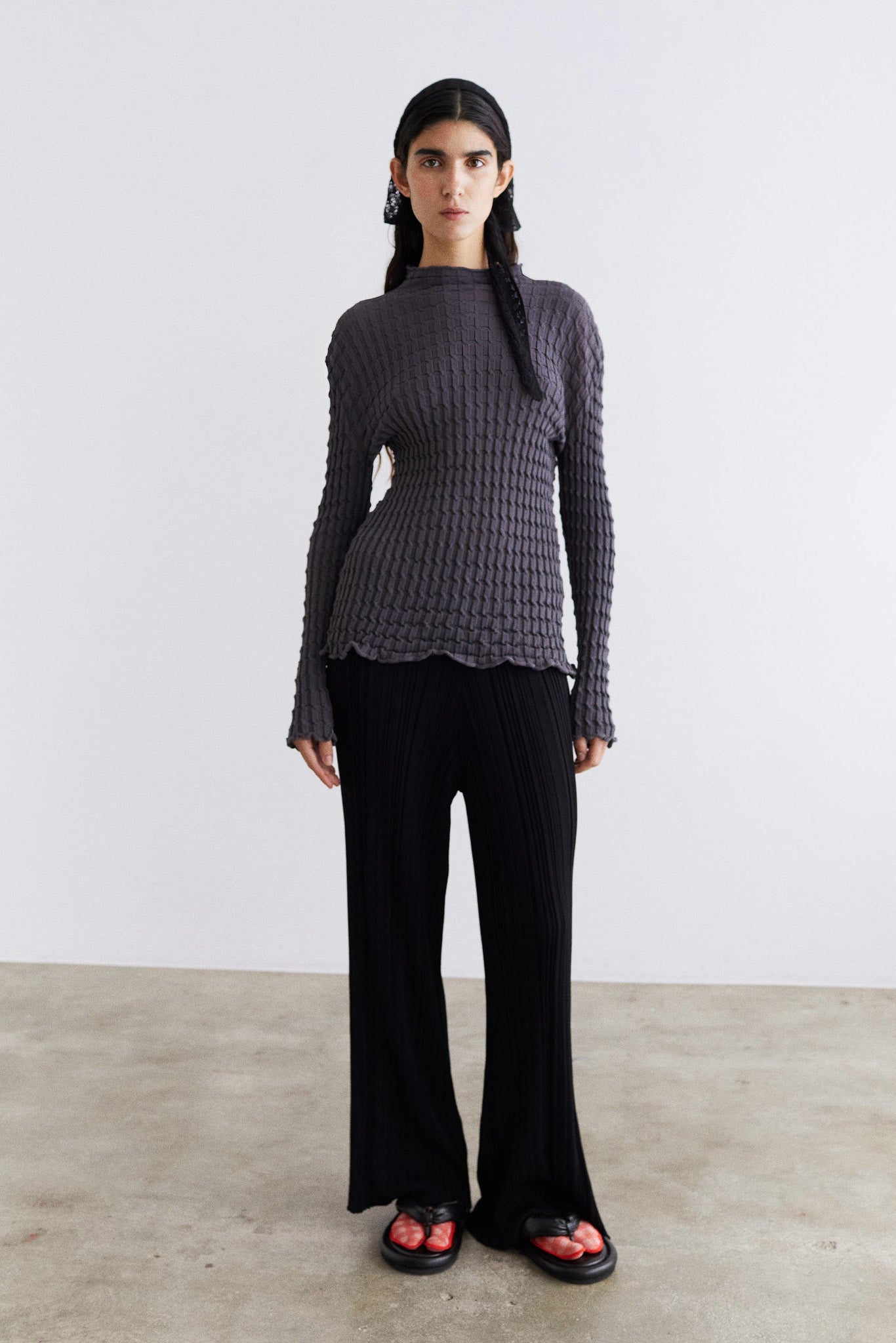 Person wearing a dark ribbed sweater and black pants on a plain background