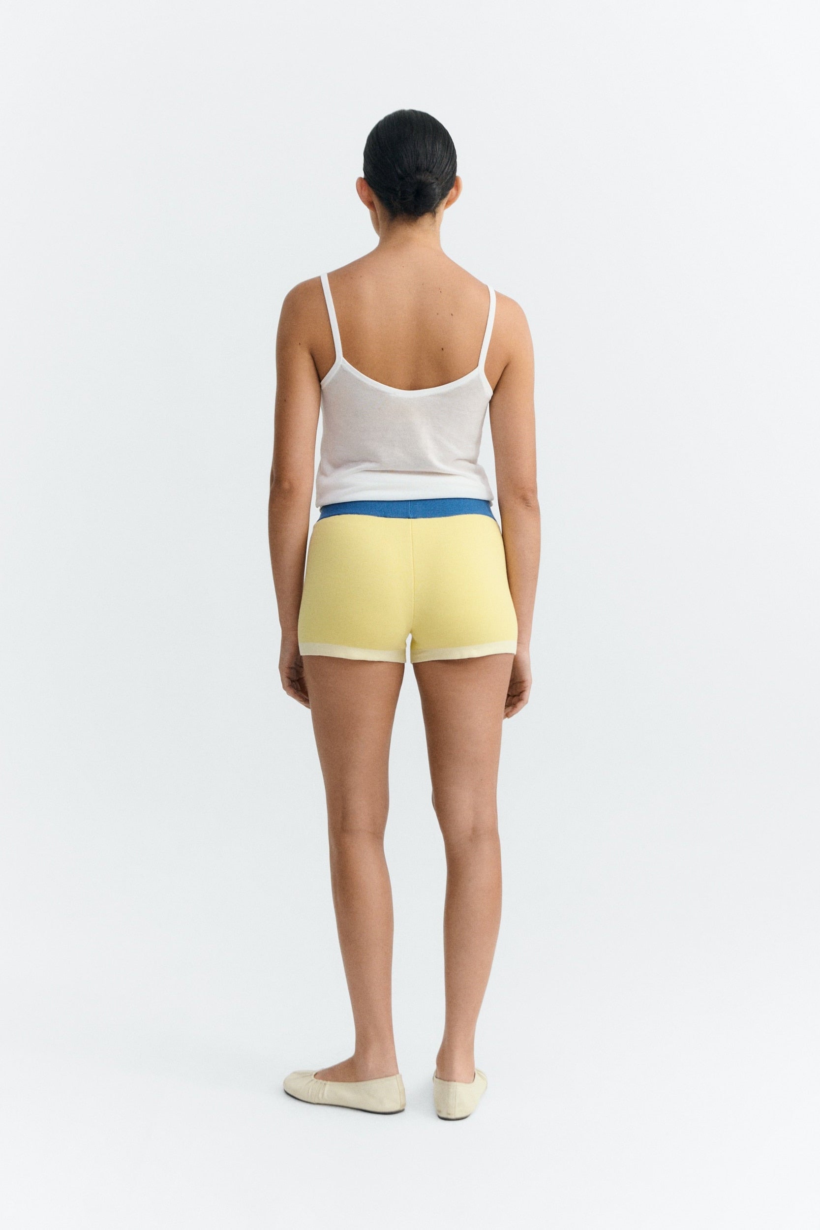Person wearing a white tank top and yellow shorts with a blue waistband on a white background