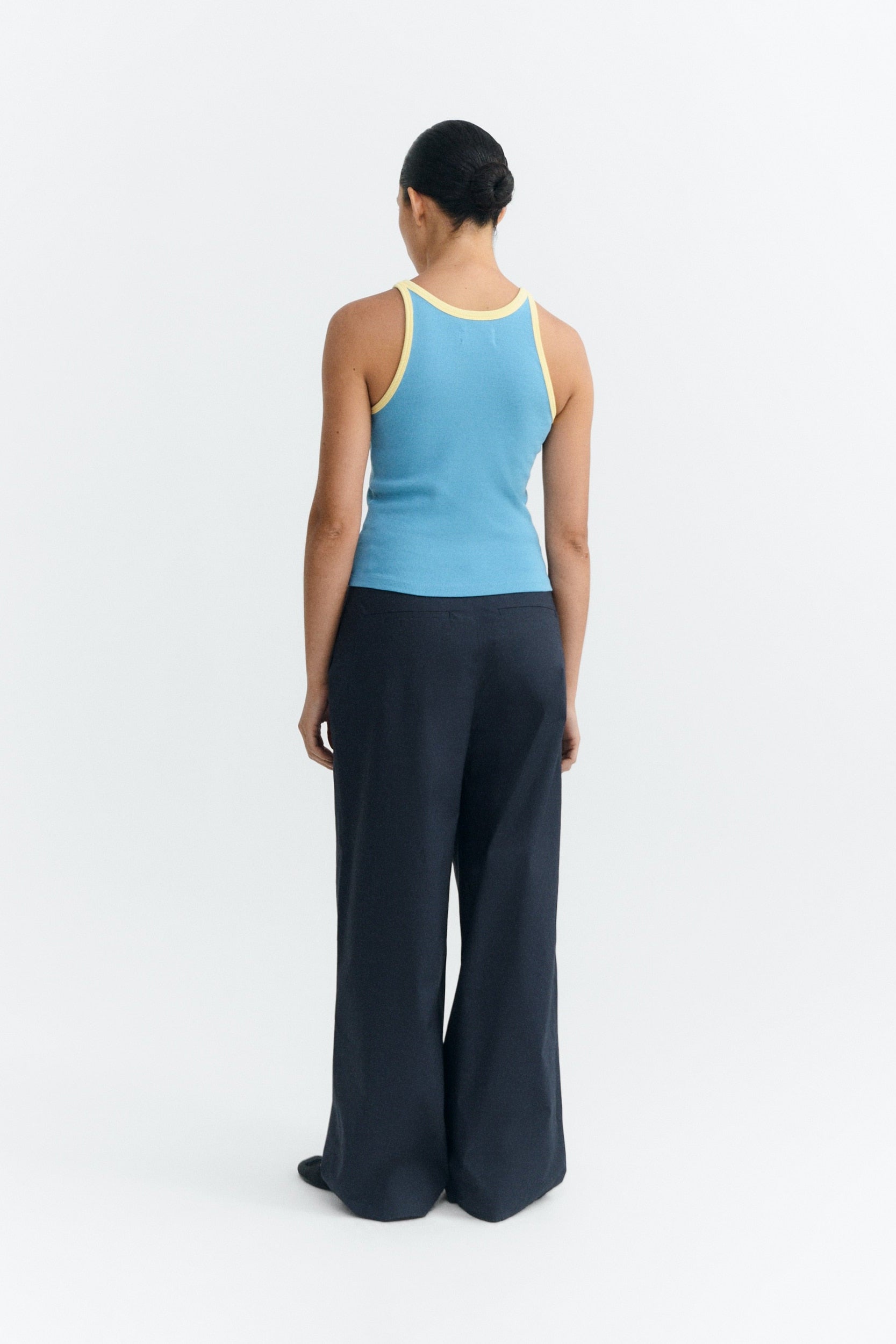 Person wearing a blue tank top and dark pants on a white background