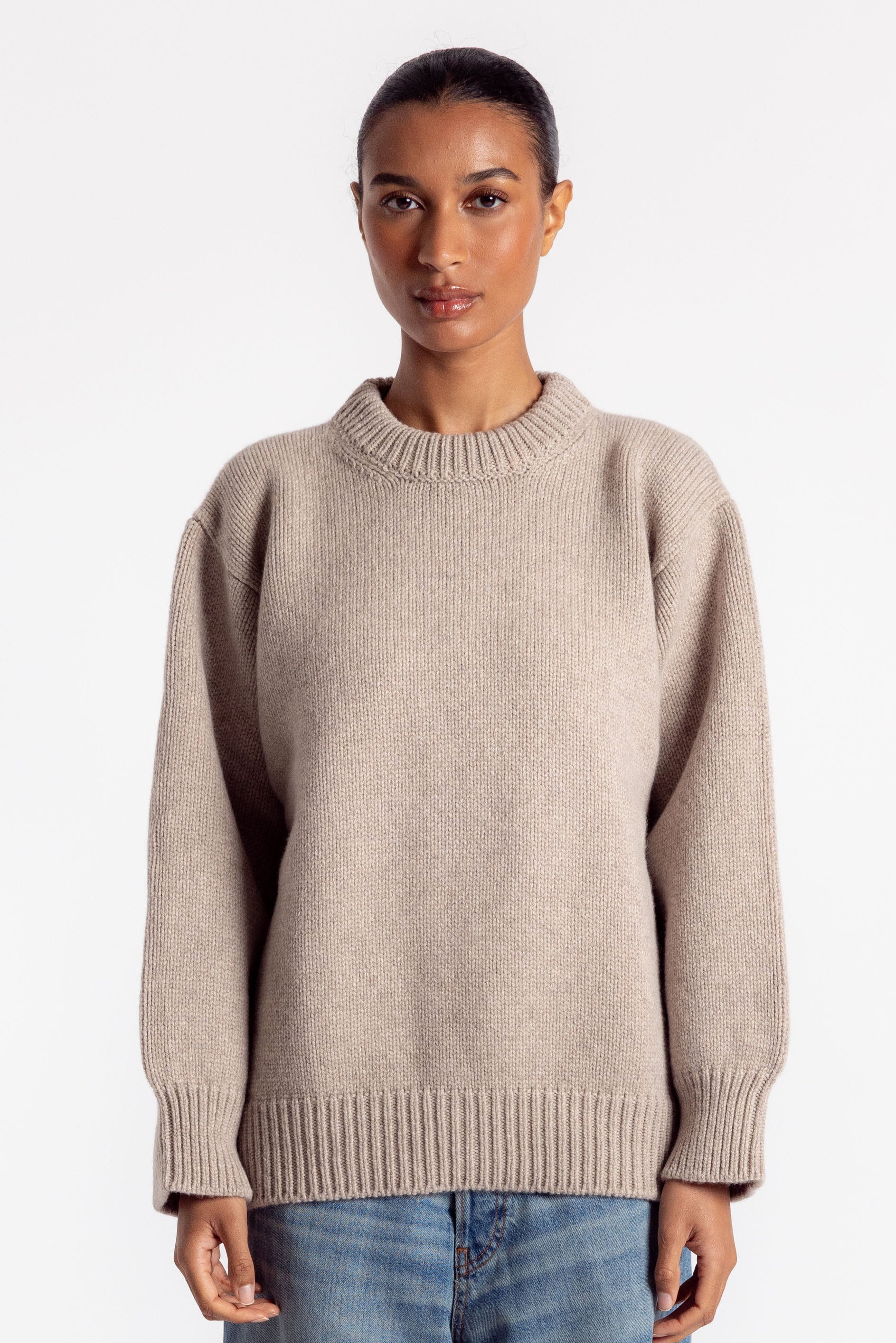 Person wearing a beige sweater and blue jeans on a white background