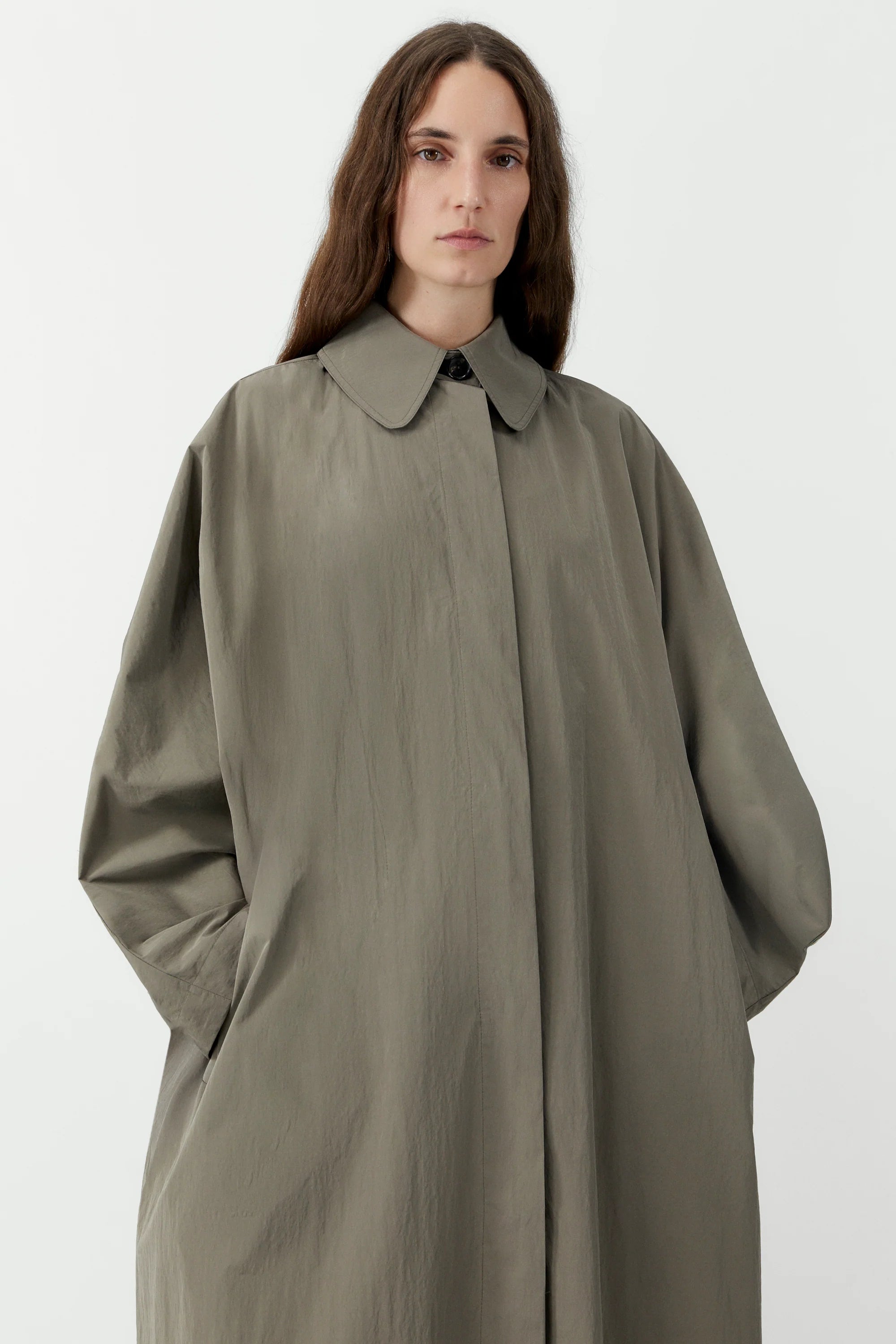 Woman wearing a long olive green coat on a white background