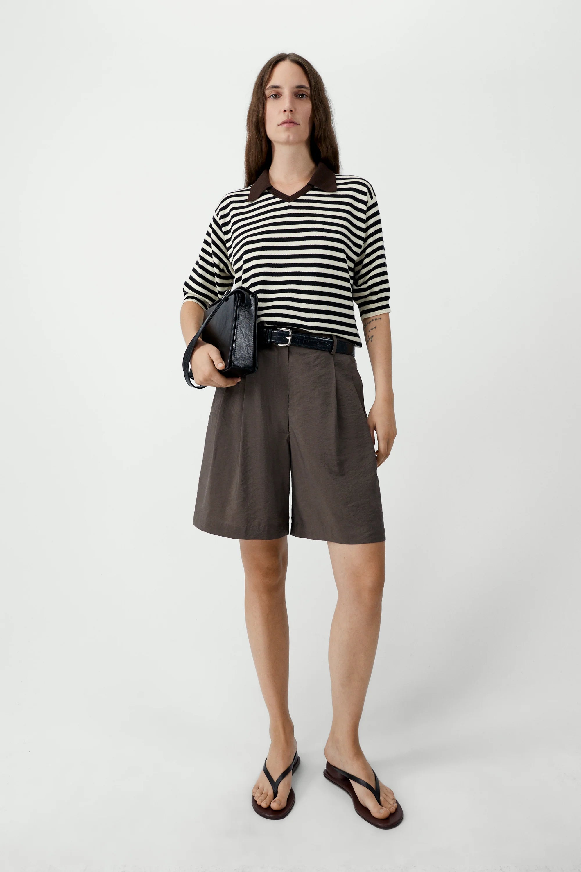 Person wearing a black and white striped shirt with brown shorts on a white background