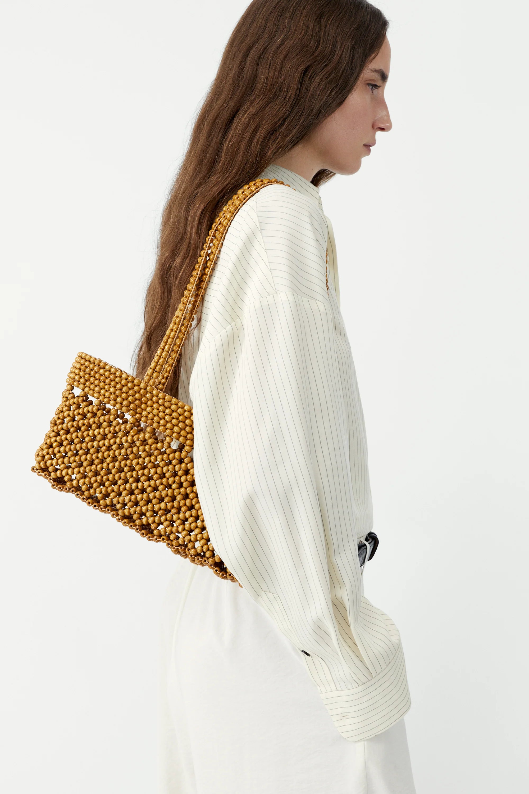 Woman carrying a mustard yellow beaded handbag on a white background