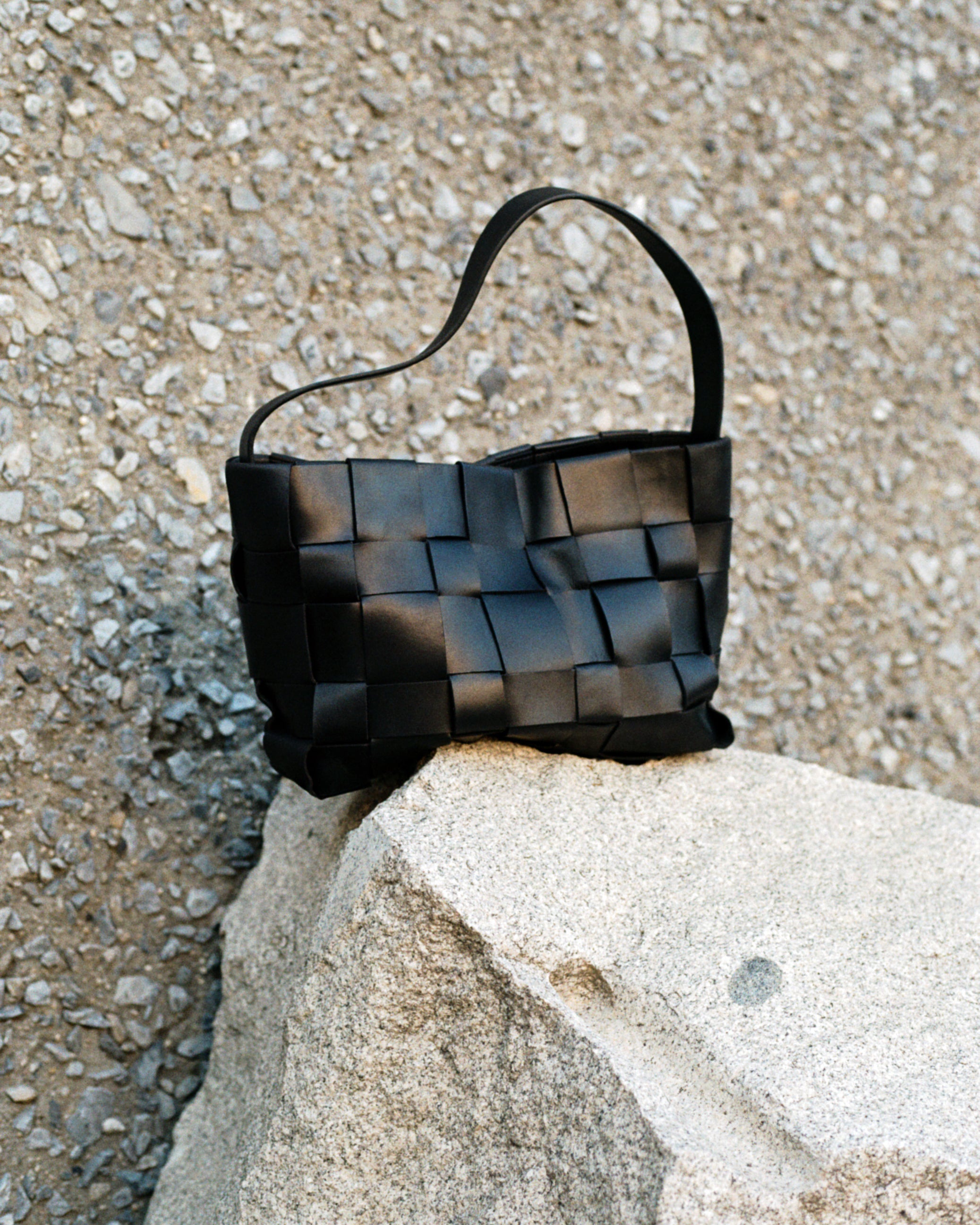 Black woven handbag on a stone surface with a textured background