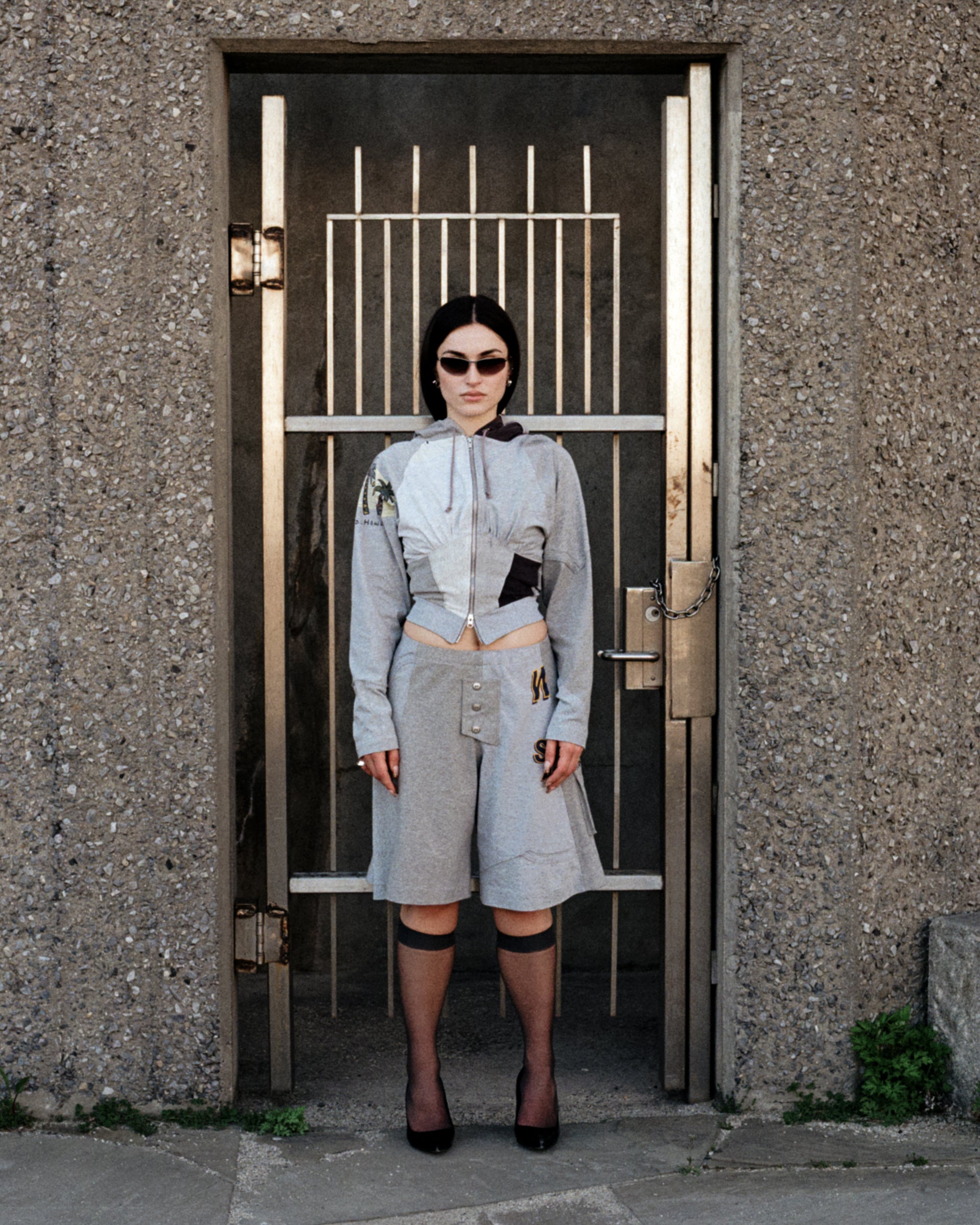 Person wearing a light gray outfit standing in front of a metal gate.
