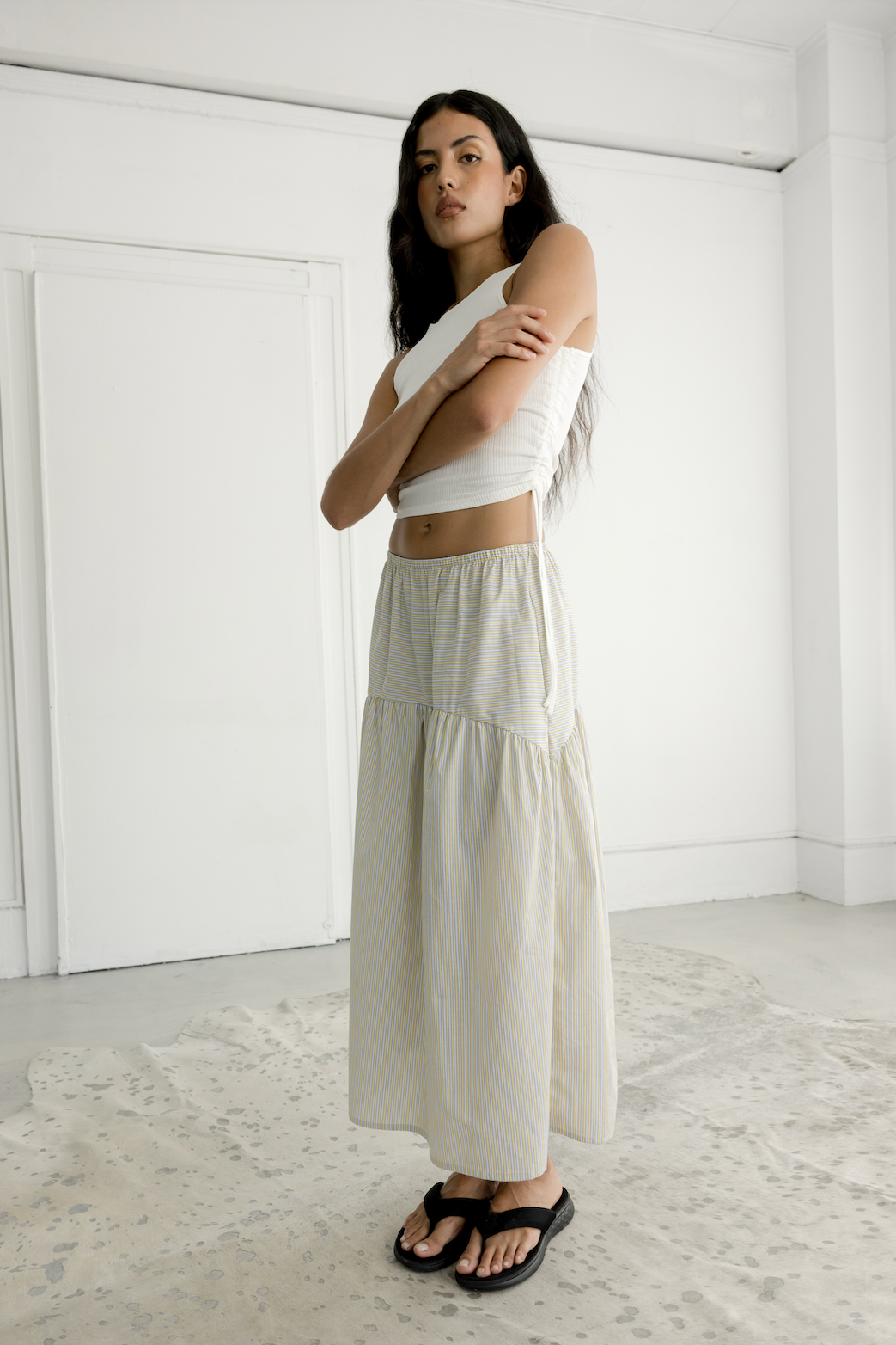 Woman wearing a white top and beige skirt in a minimalistic room.