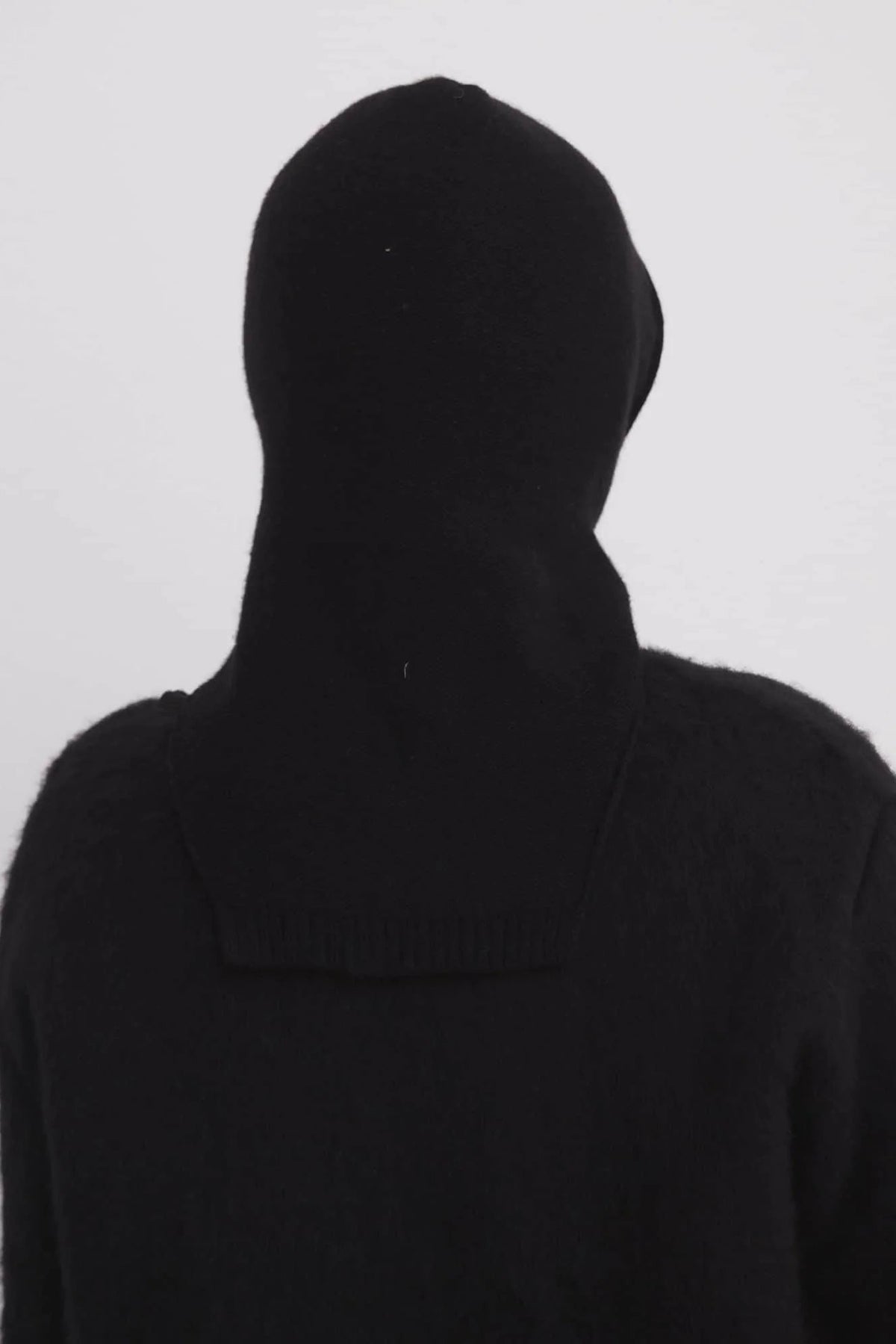 Person wearing a black hooded garment against a white background