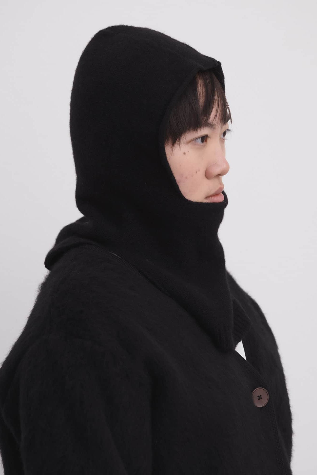 Person wearing a black hooded coat against a white background