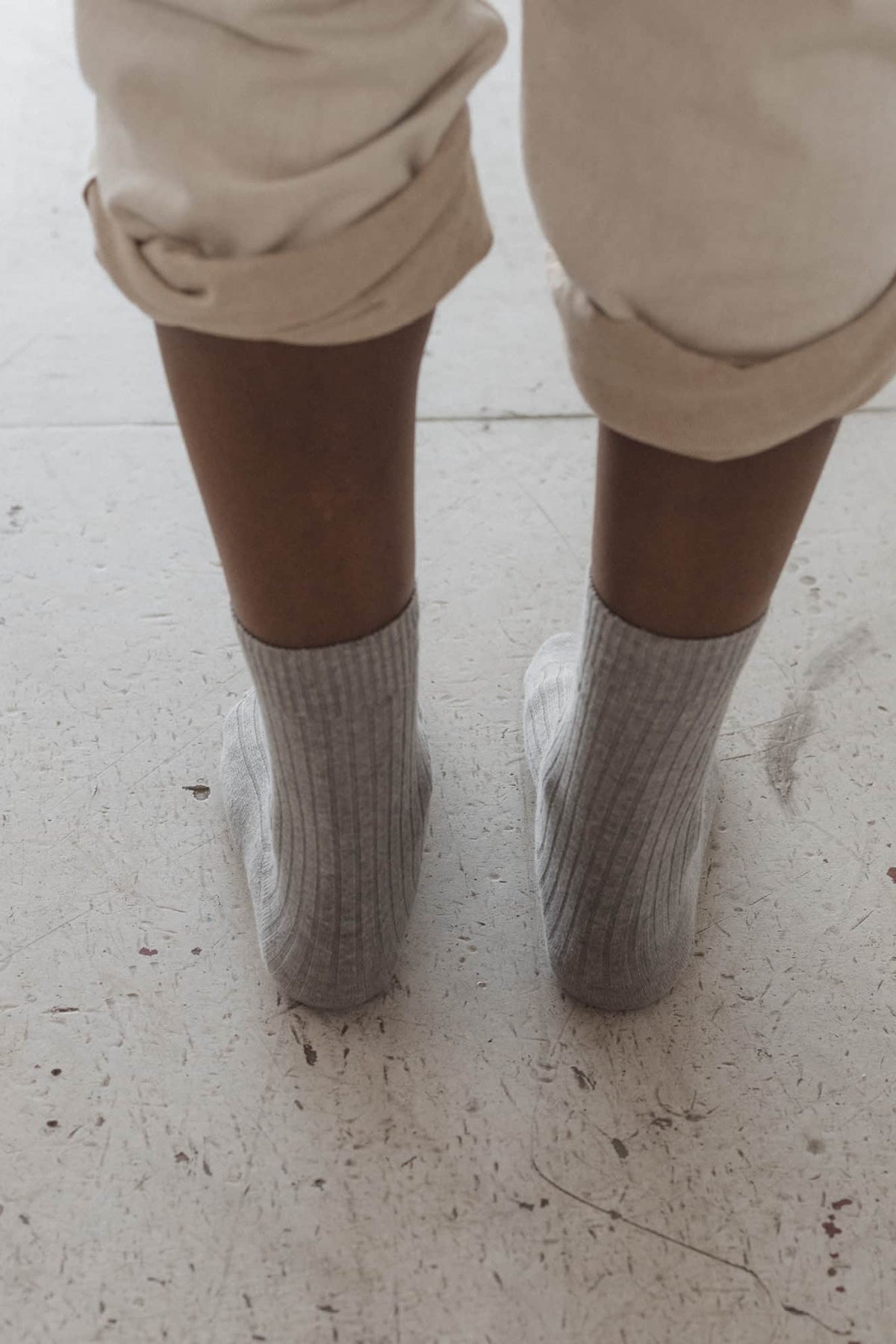 Close-up of a person wearing beige pants and gray socks on a light-colored floor.