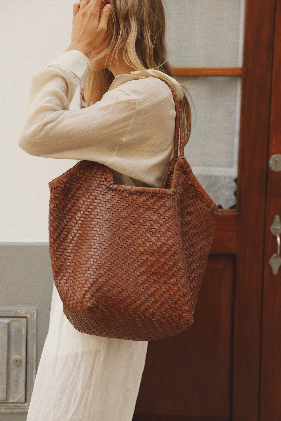 Person holding a woven brown bag in front of a wooden door.