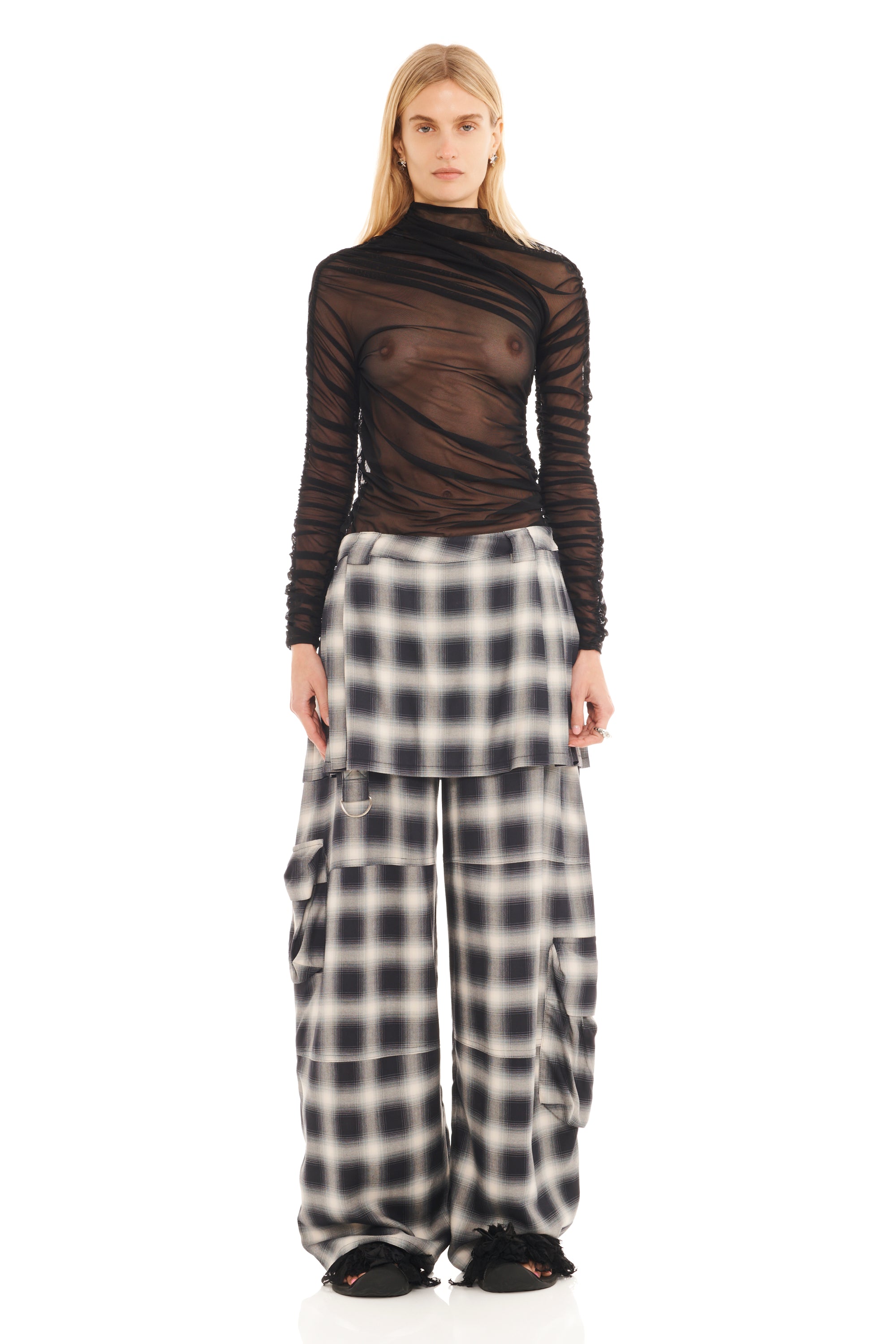 Person wearing a brown sheer top and plaid pants on a white background