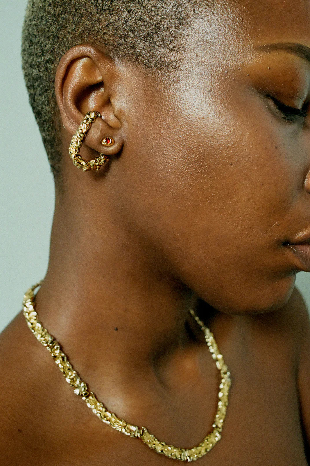 Close-up of a person wearing gold earrings and necklace against a neutral background