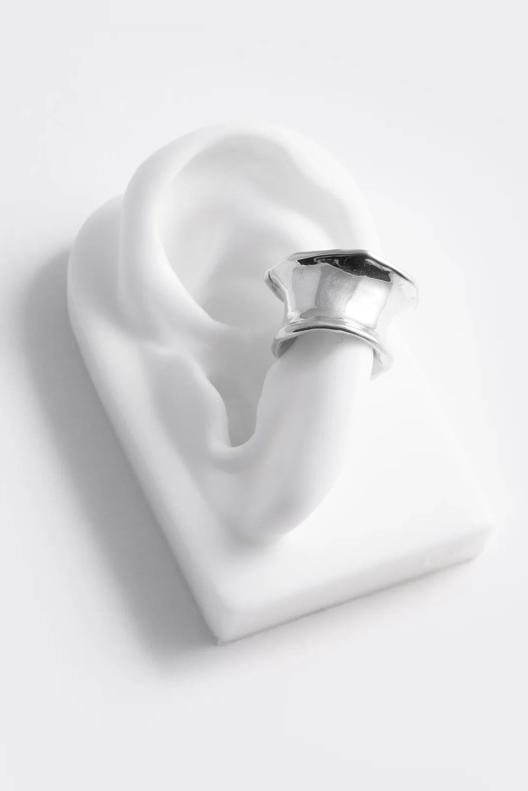 Heart-shaped white ceramic object with a metallic handle on a light gray background