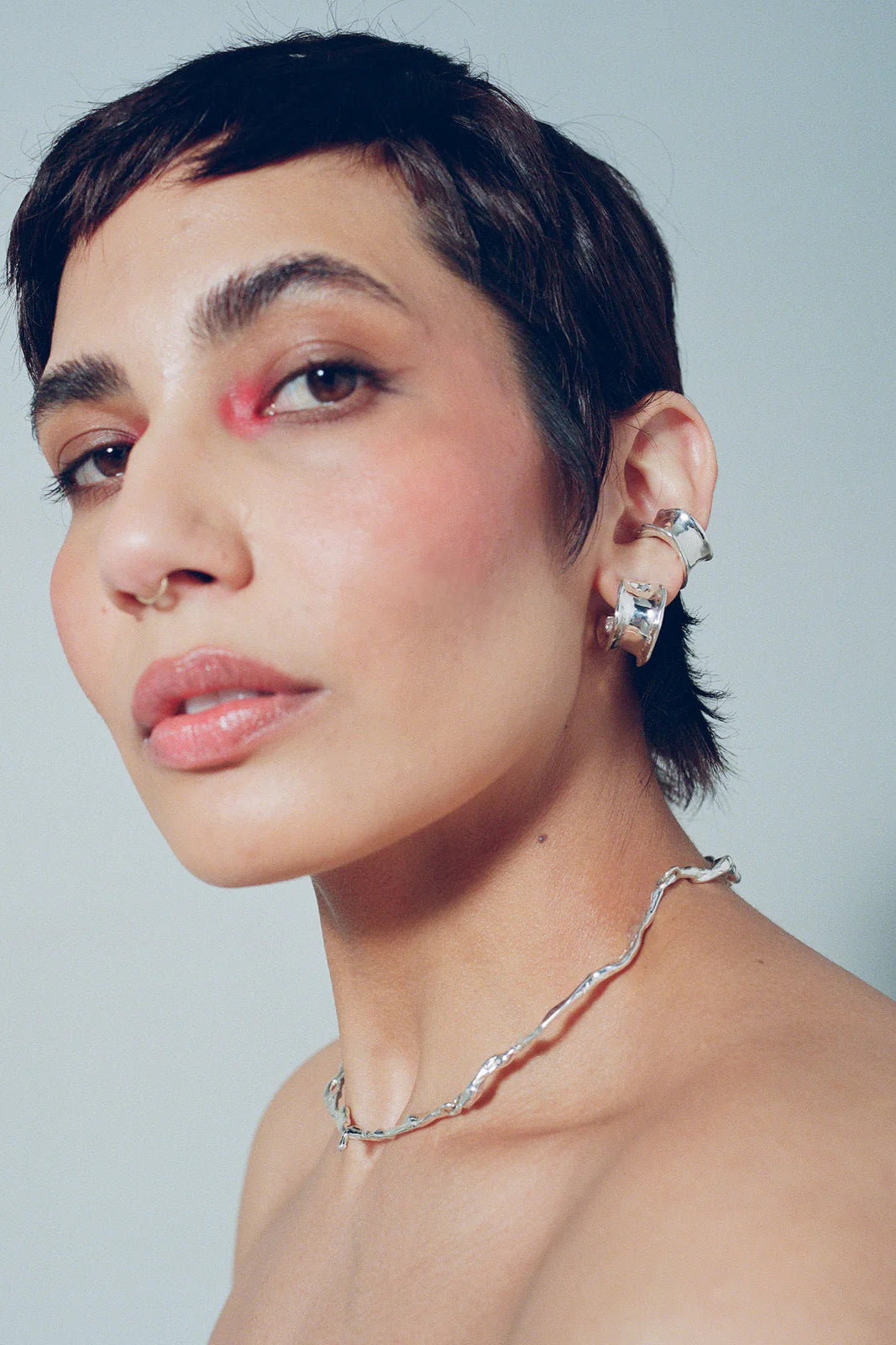 Woman wearing earrings and a necklace against a plain background