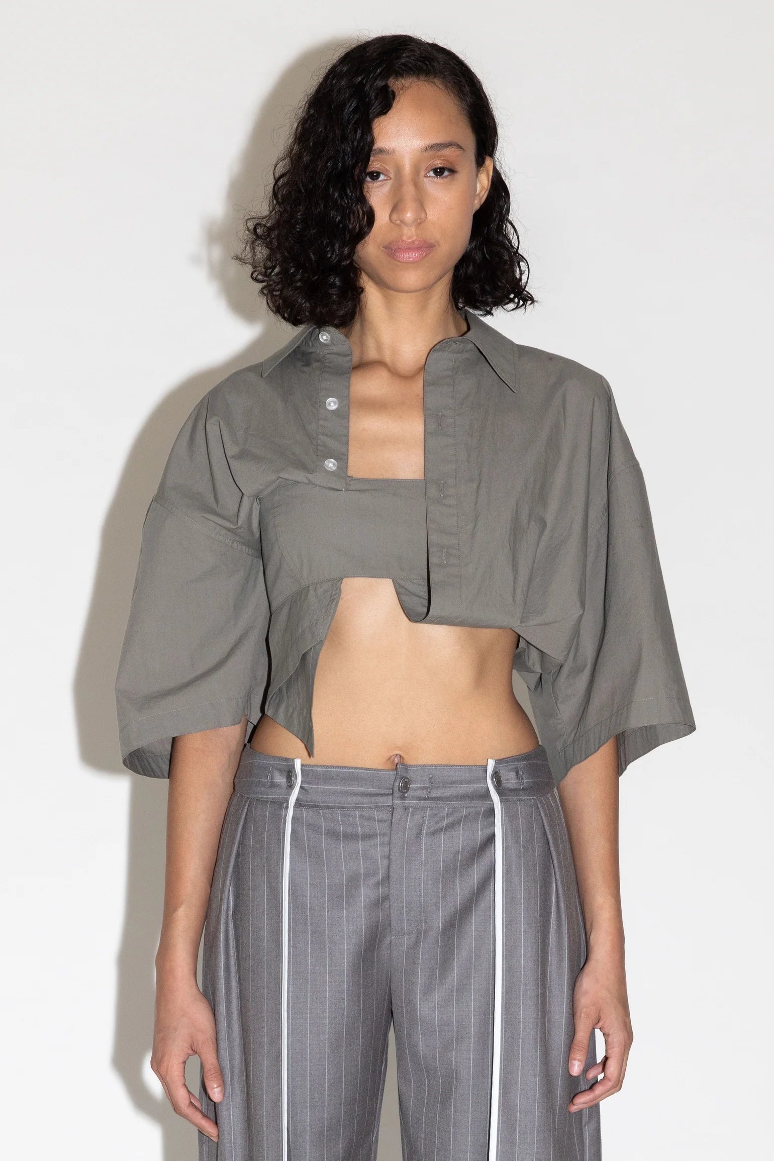 Woman wearing a gray outfit with a cropped top and pants against a white background