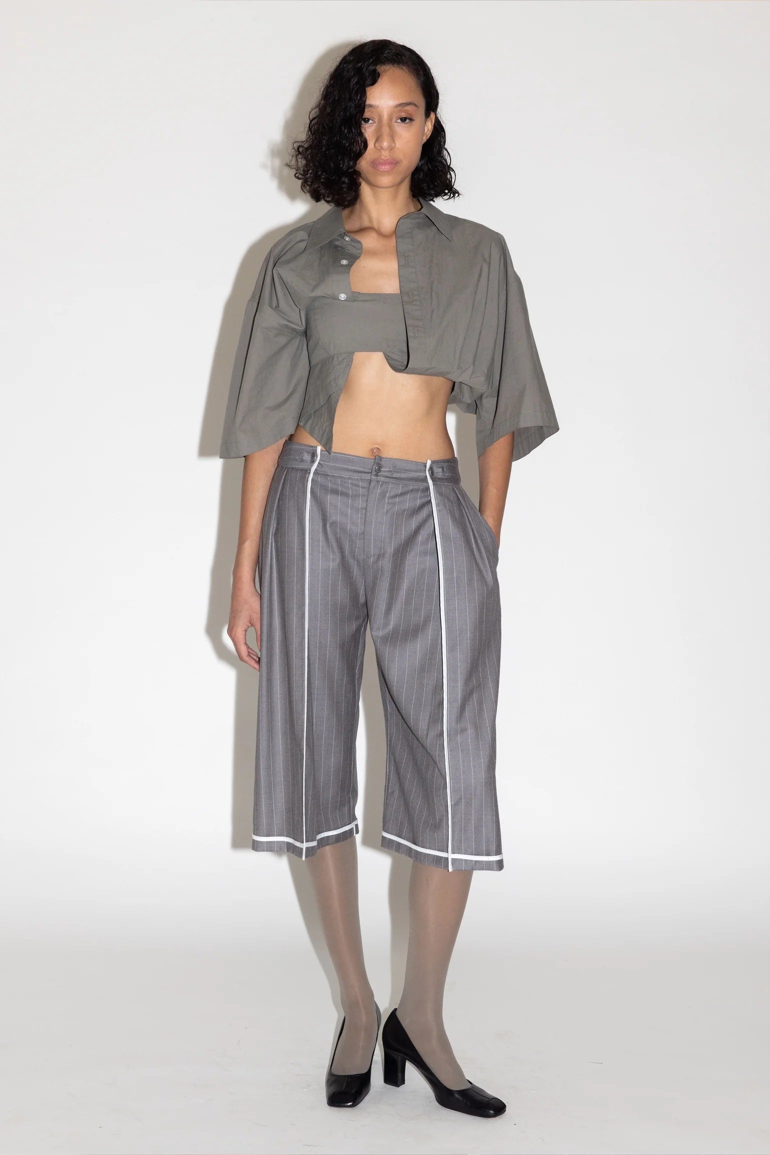 Woman wearing a gray outfit with cropped jacket and striped pants on a white background