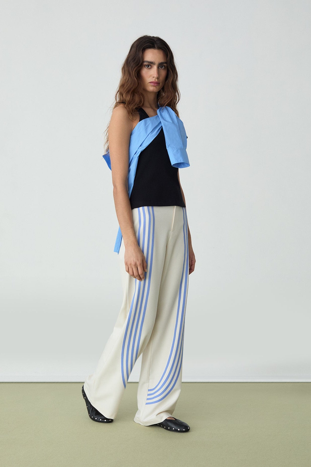 Woman wearing a black top, blue and white striped pants, and a blue jacket on a white background