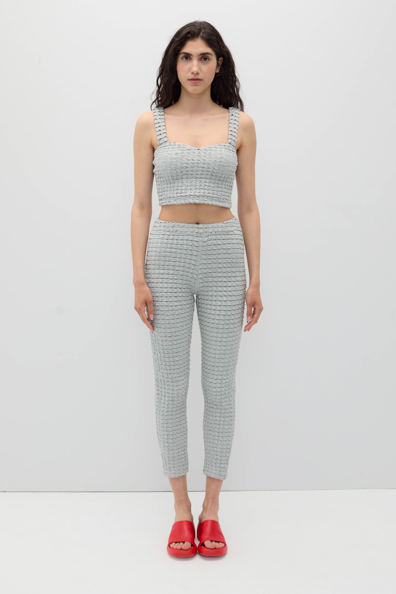 Woman wearing a gray textured outfit with red shoes on a white background