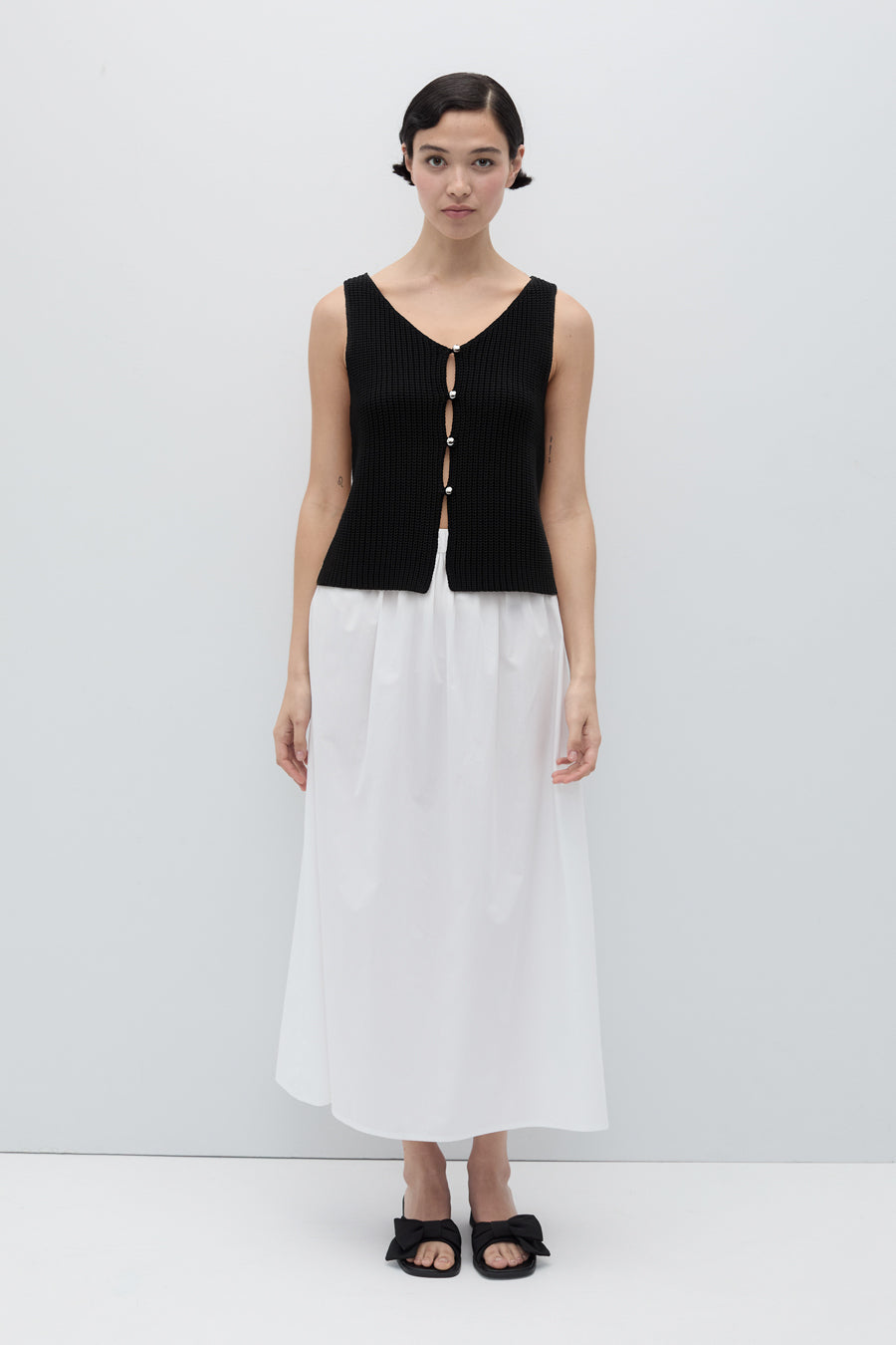 Woman wearing a black sleeveless top and white skirt on a white background