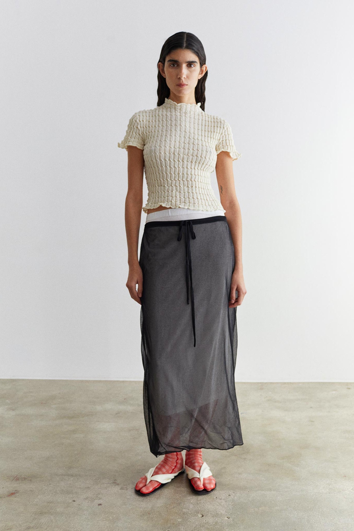 Woman wearing a white textured top and gray skirt on a plain background