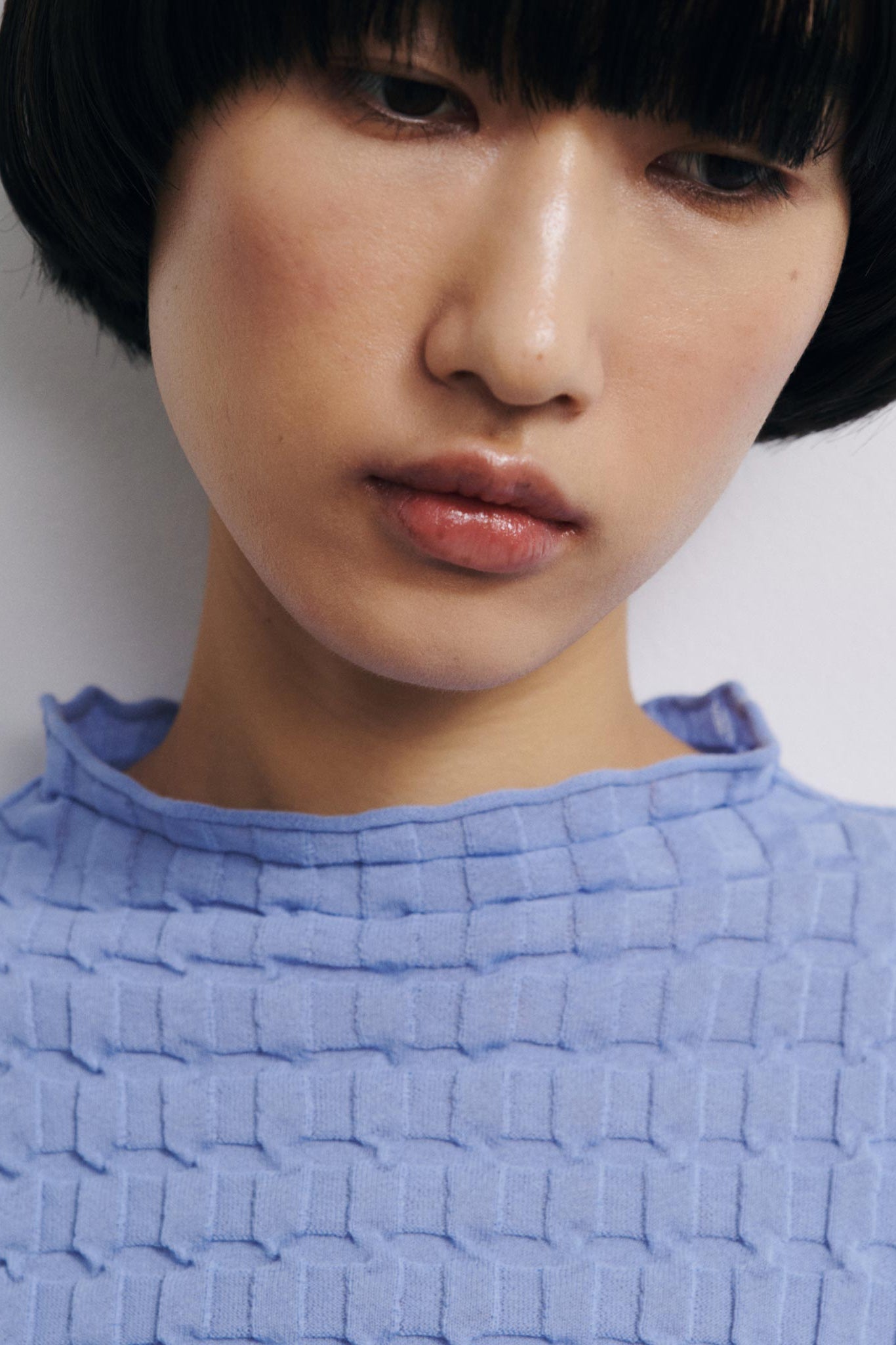 Person wearing a textured blue top against a plain background