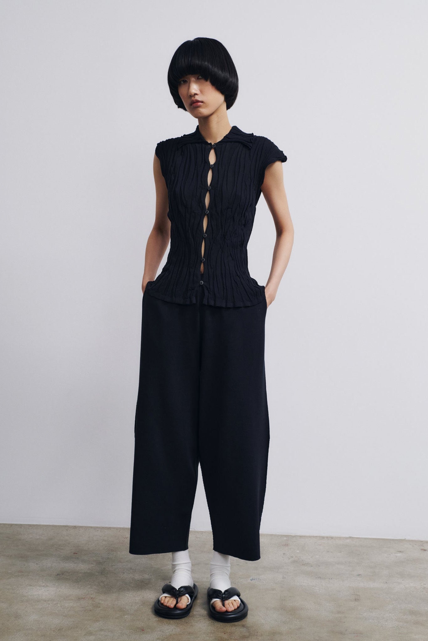 Person wearing a black sleeveless top and wide-leg pants against a plain background
