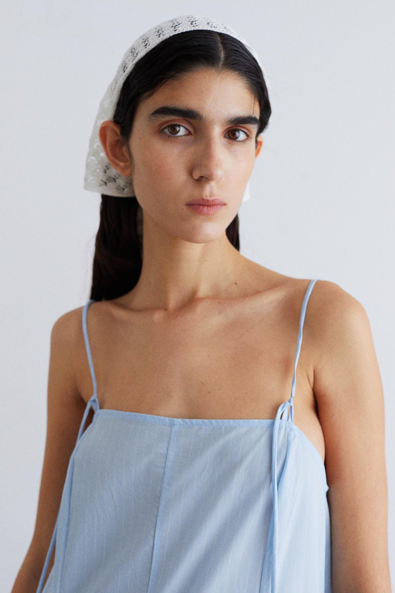 Woman wearing a light blue dress with thin straps against a plain background