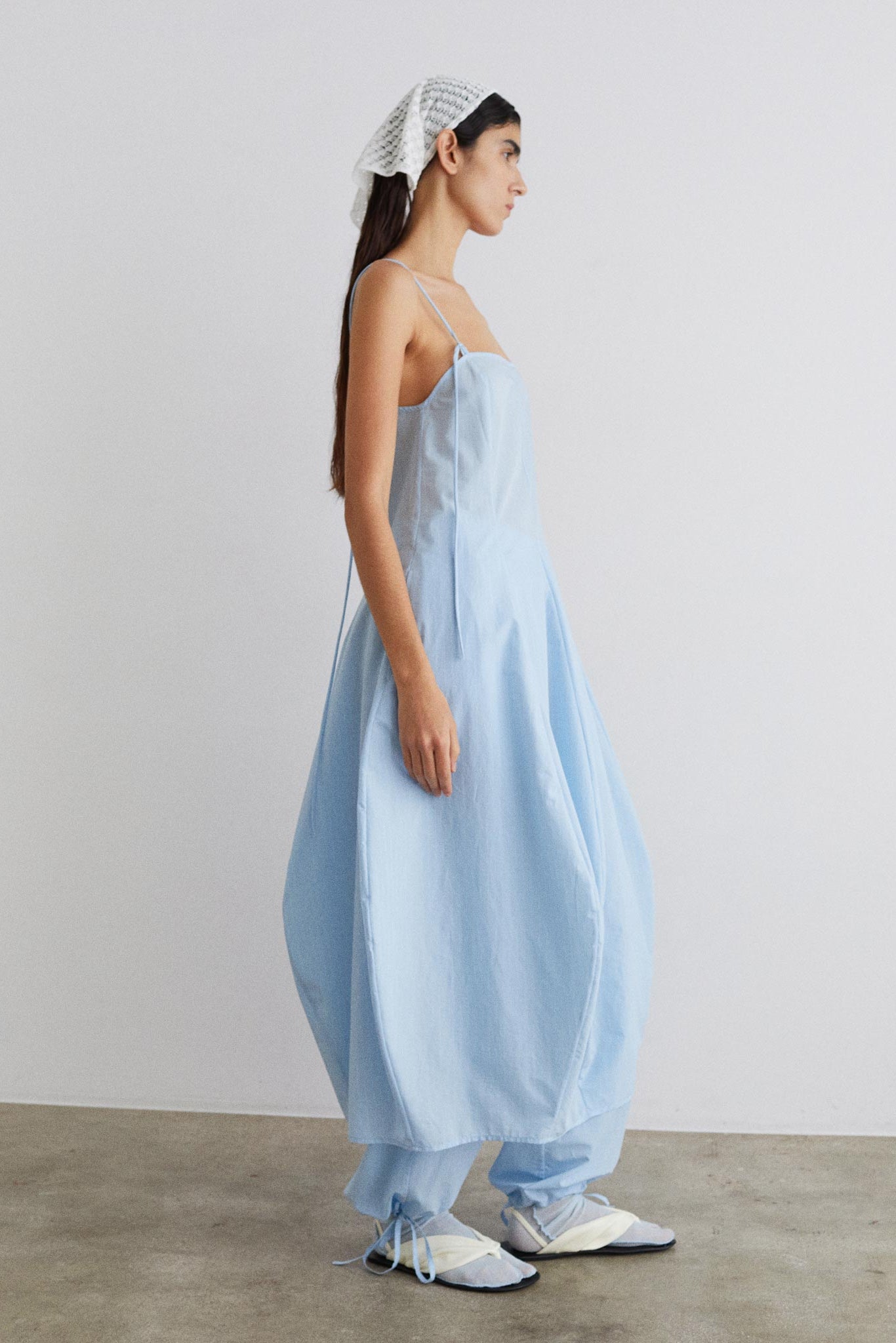 Woman wearing a light blue dress with a white headscarf against a plain background