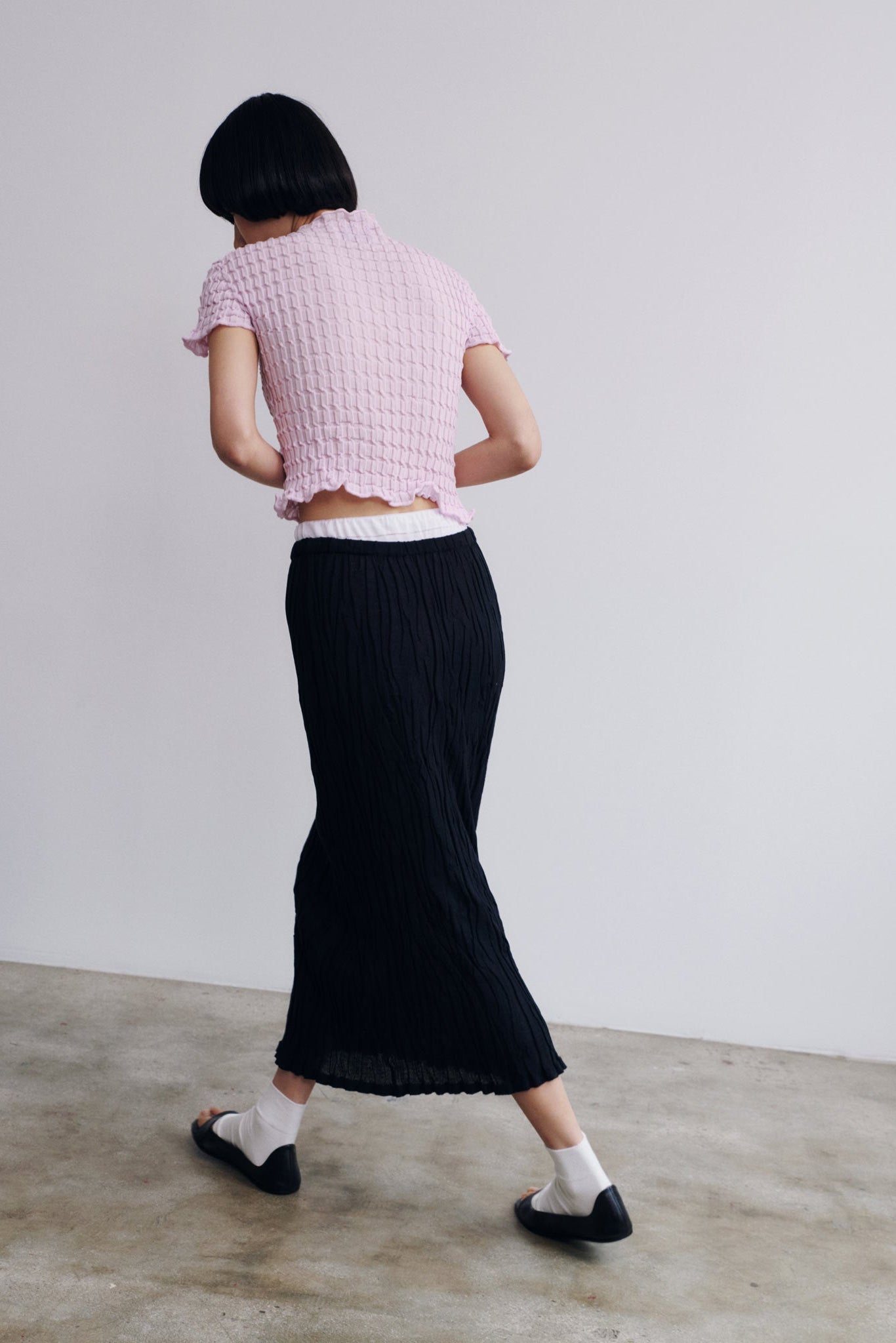 Person wearing a pink textured top and black skirt against a plain background