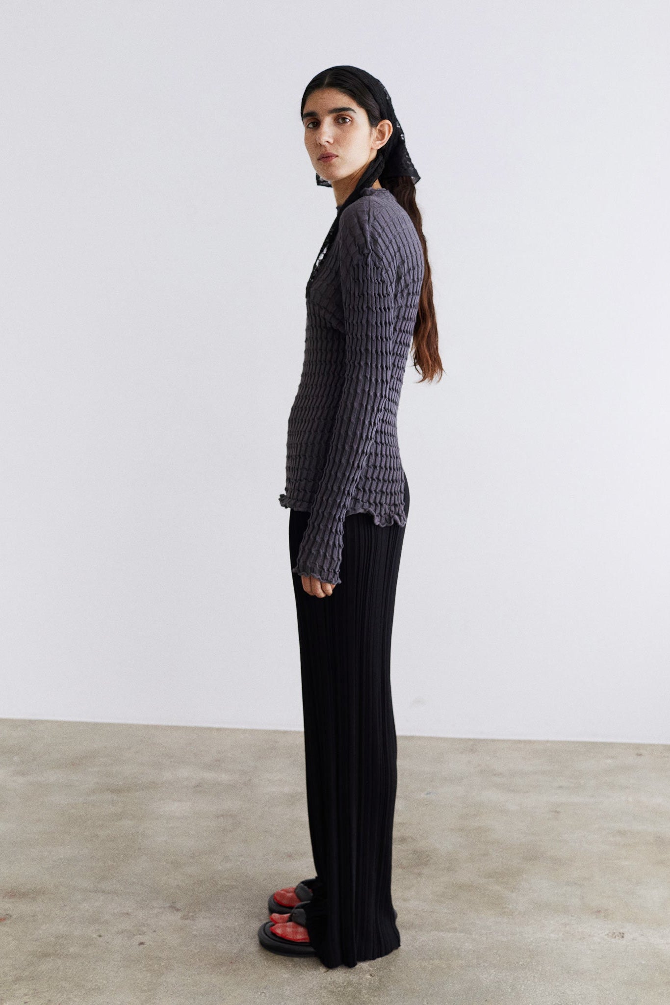 Woman wearing a ribbed sweater and black pants standing against a white wall.