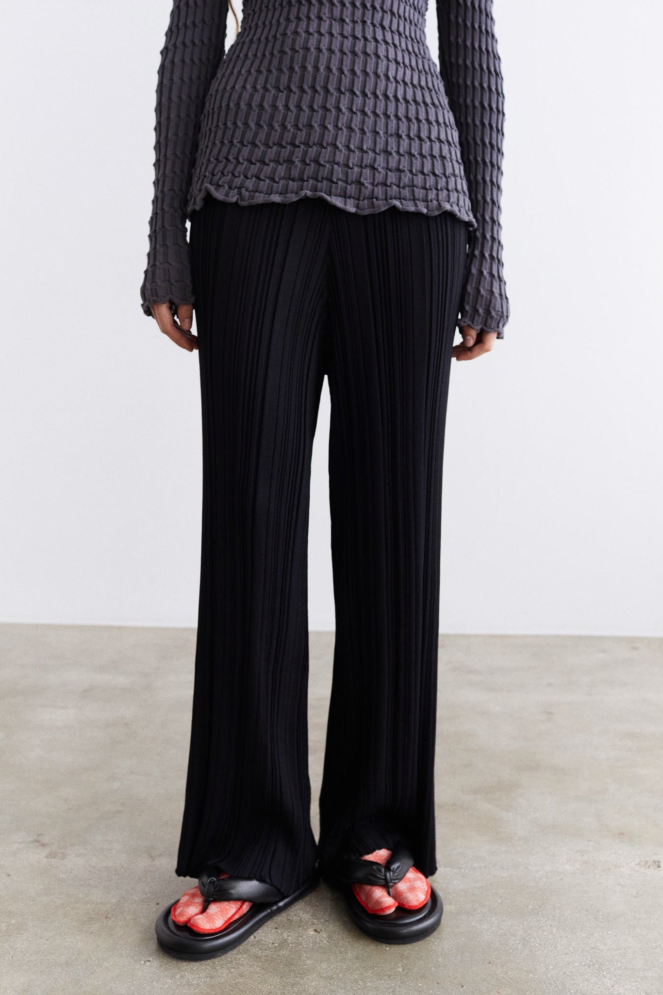 Person wearing a textured gray top and black wide-leg pants on a plain background