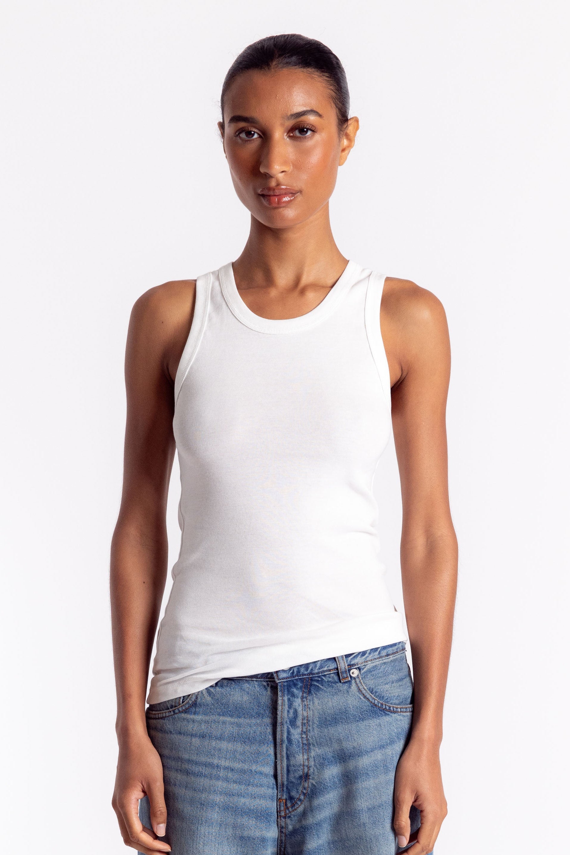 Woman wearing a white tank top and blue jeans on a white background