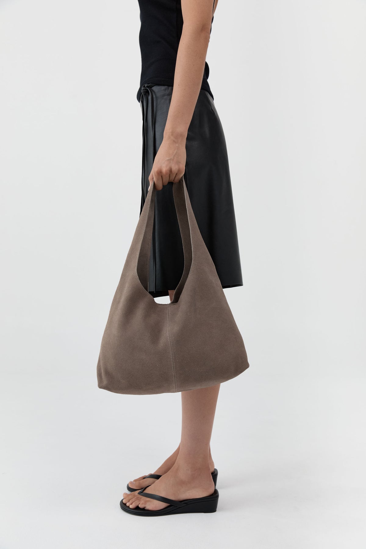 Person holding a brown suede handbag on a white background