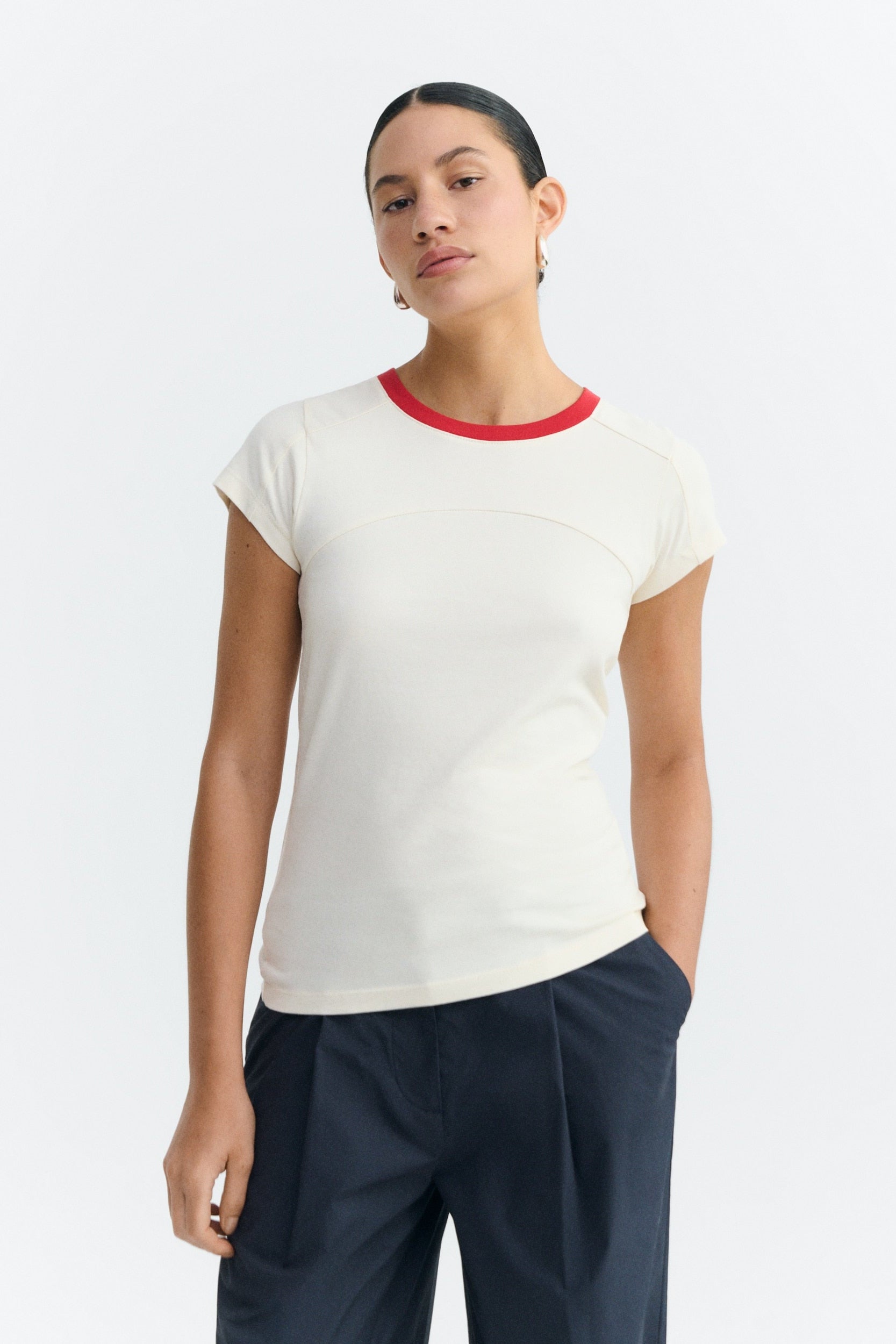 Person wearing a white t-shirt with red trim and navy pants on a white background